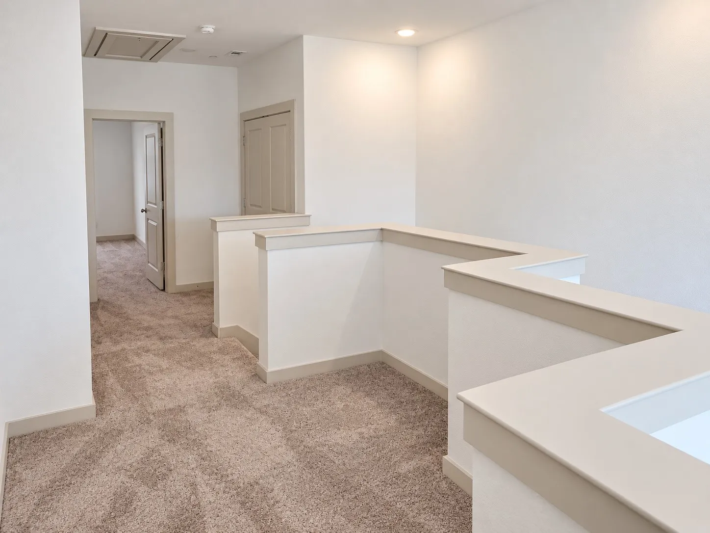 Carpeted hallway with painted walls and trim, featuring recessed ceiling lighting, and a partial hallway railing