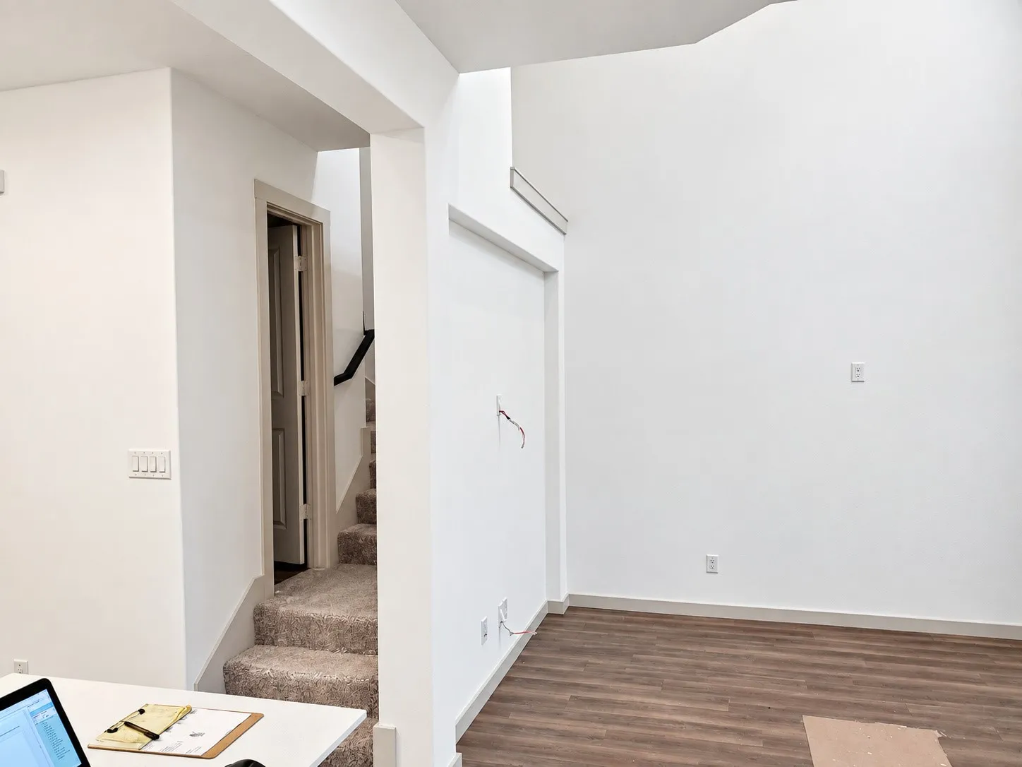 Expansive interior with high ceilings, wood-finish flooring, and a carpeted staircase with a black handrail