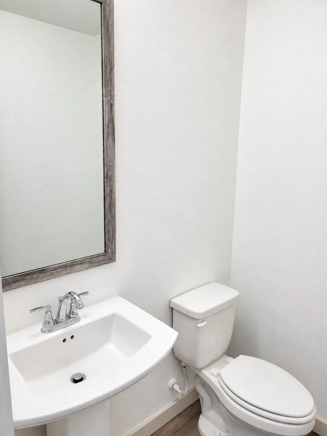 Pedestal sink with chrome faucet, framed mirror, and wood-finish flooring