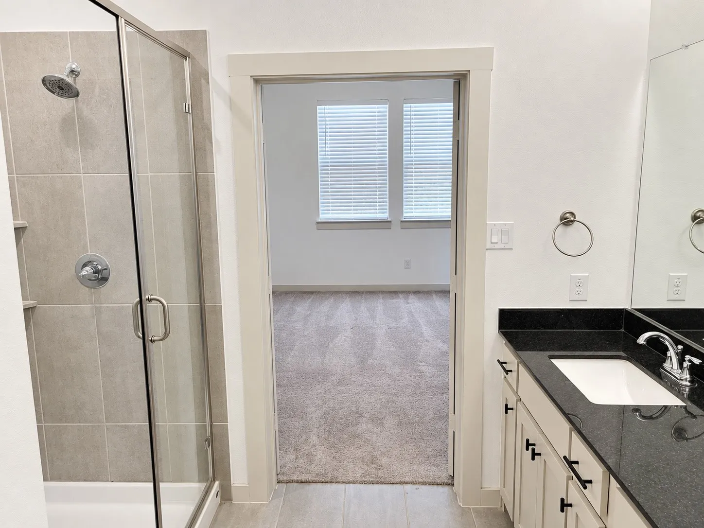 Glass-enclosed shower with subway tile surround, single vanity with black countertop, and chrome fixtures