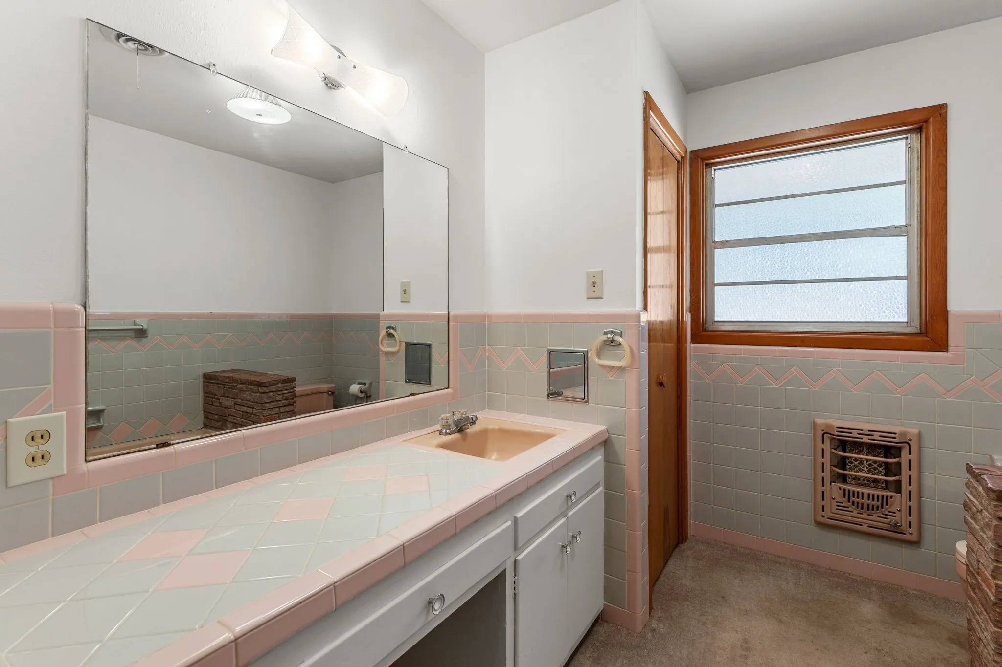 Built-in vanity with a tiled countertop, wall-mounted mirror, and vanity lighting