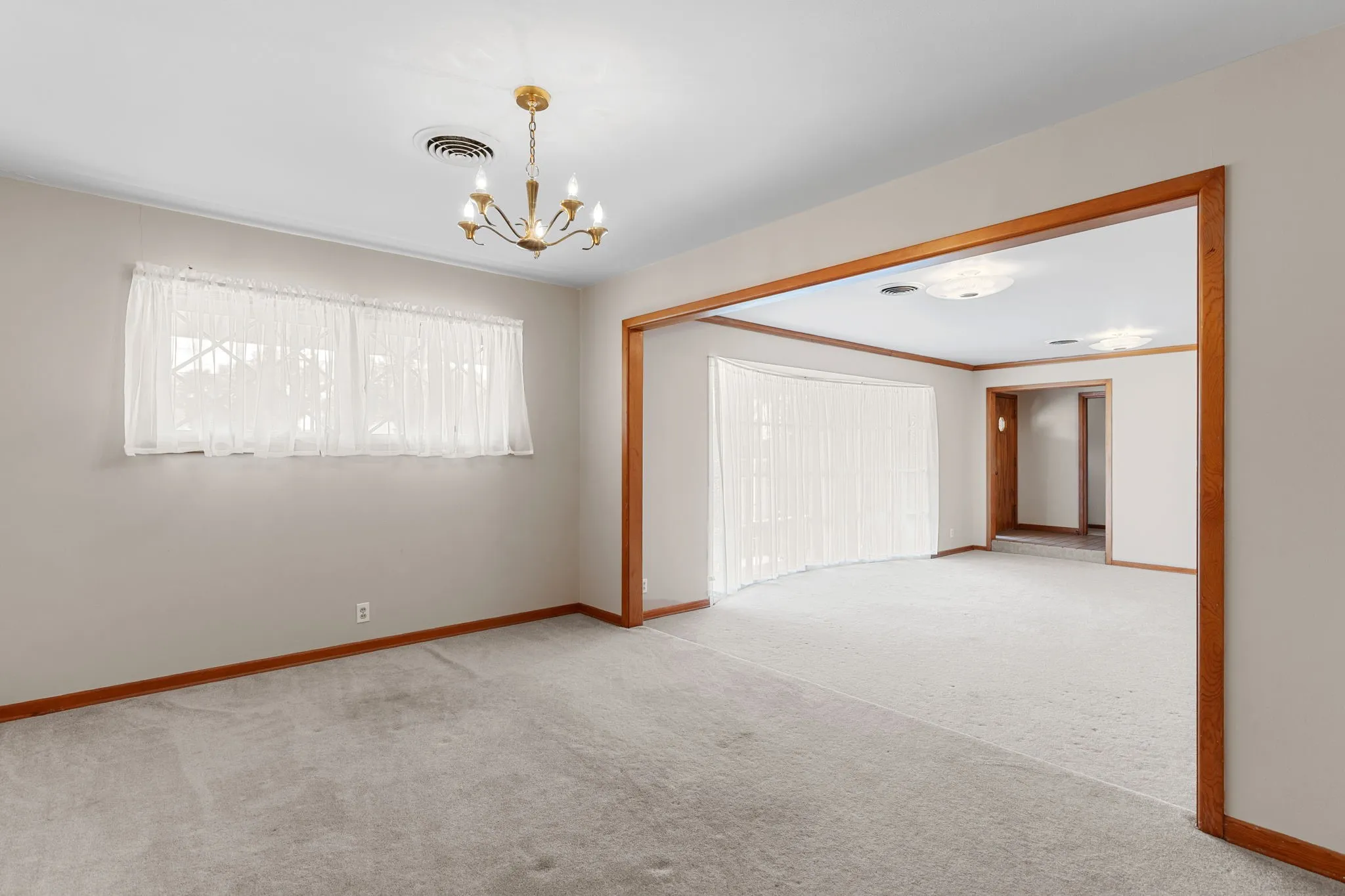 Carpeted room with a brass chandelier and a broad window