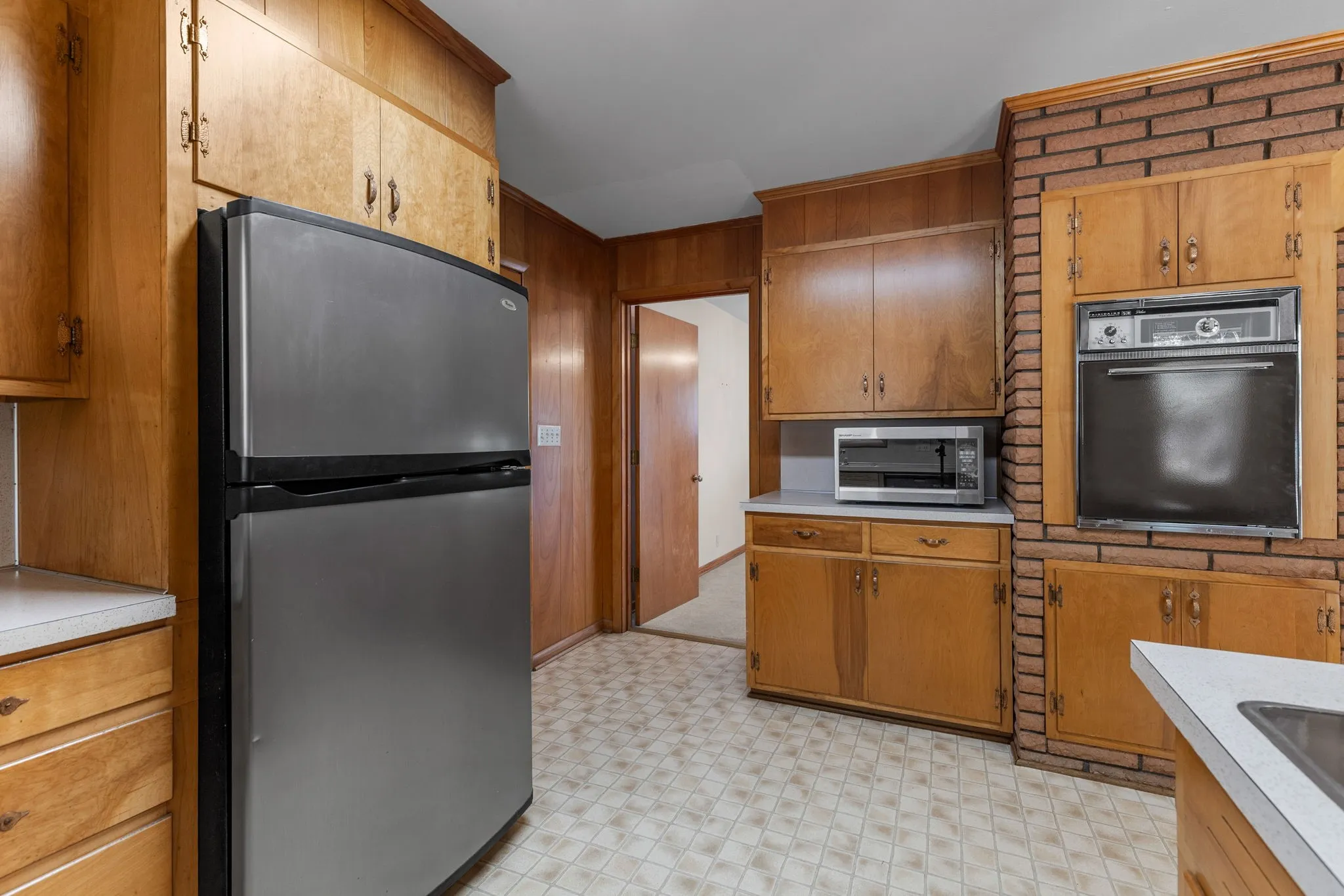 Kitchen featuring wood-paneled walls, wood cabinetry, a built-in oven, and brick detailing