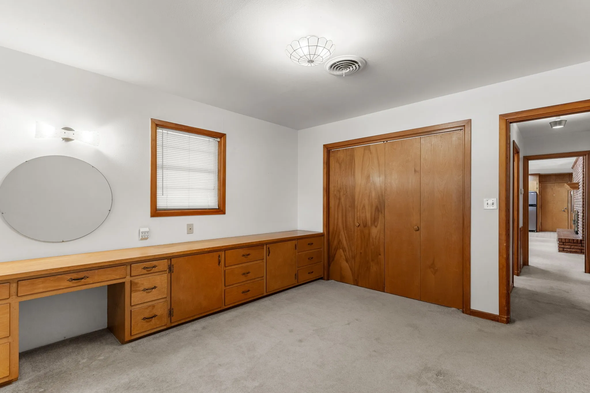 Built-in wooden cabinetry with multiple drawers, integrated desk area, and a large round mirror