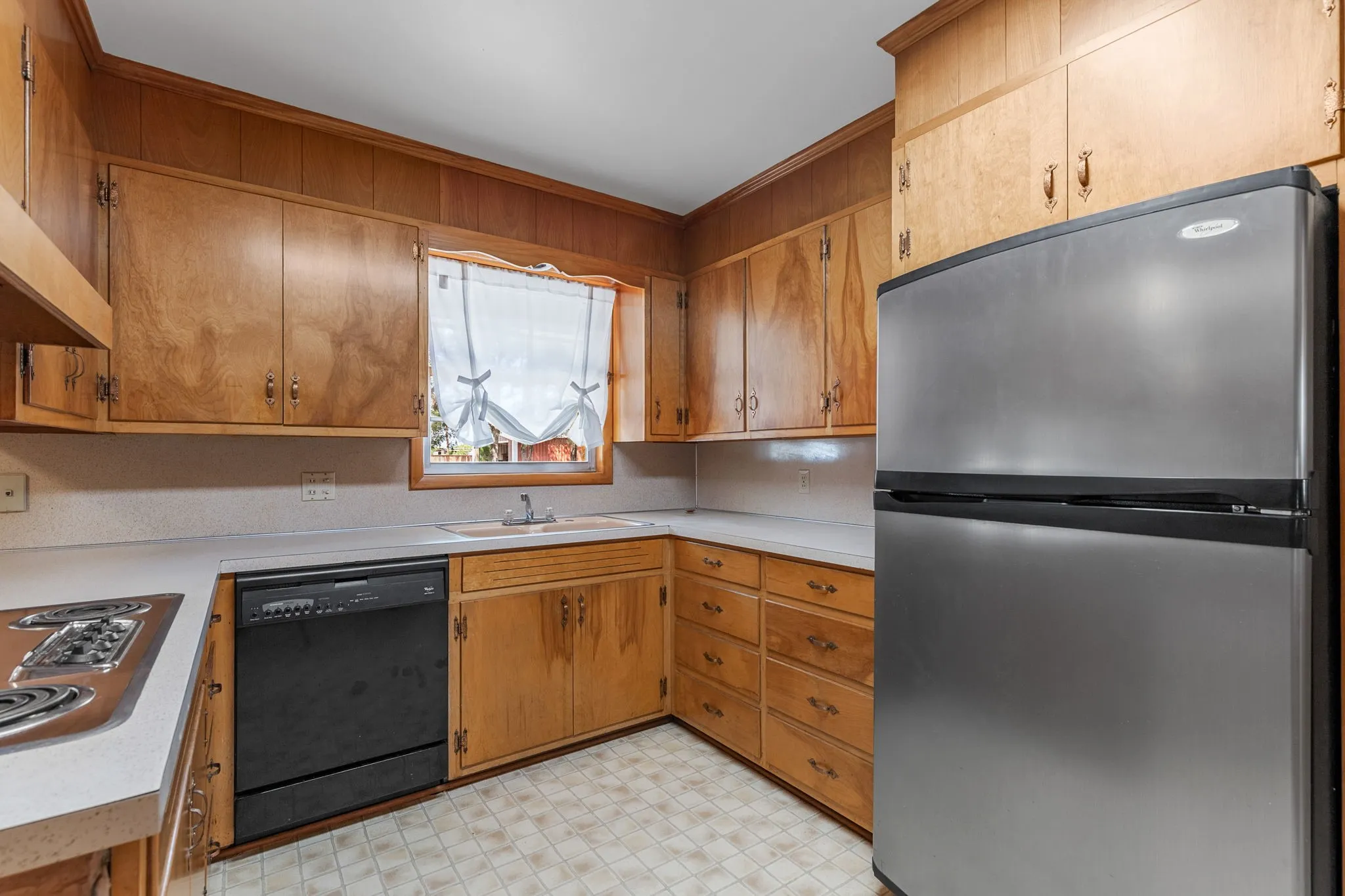 Kitchen featuring wood-paneled walls, wood cabinetry, a stainless steel refrigerator, and a built-in dishwasher