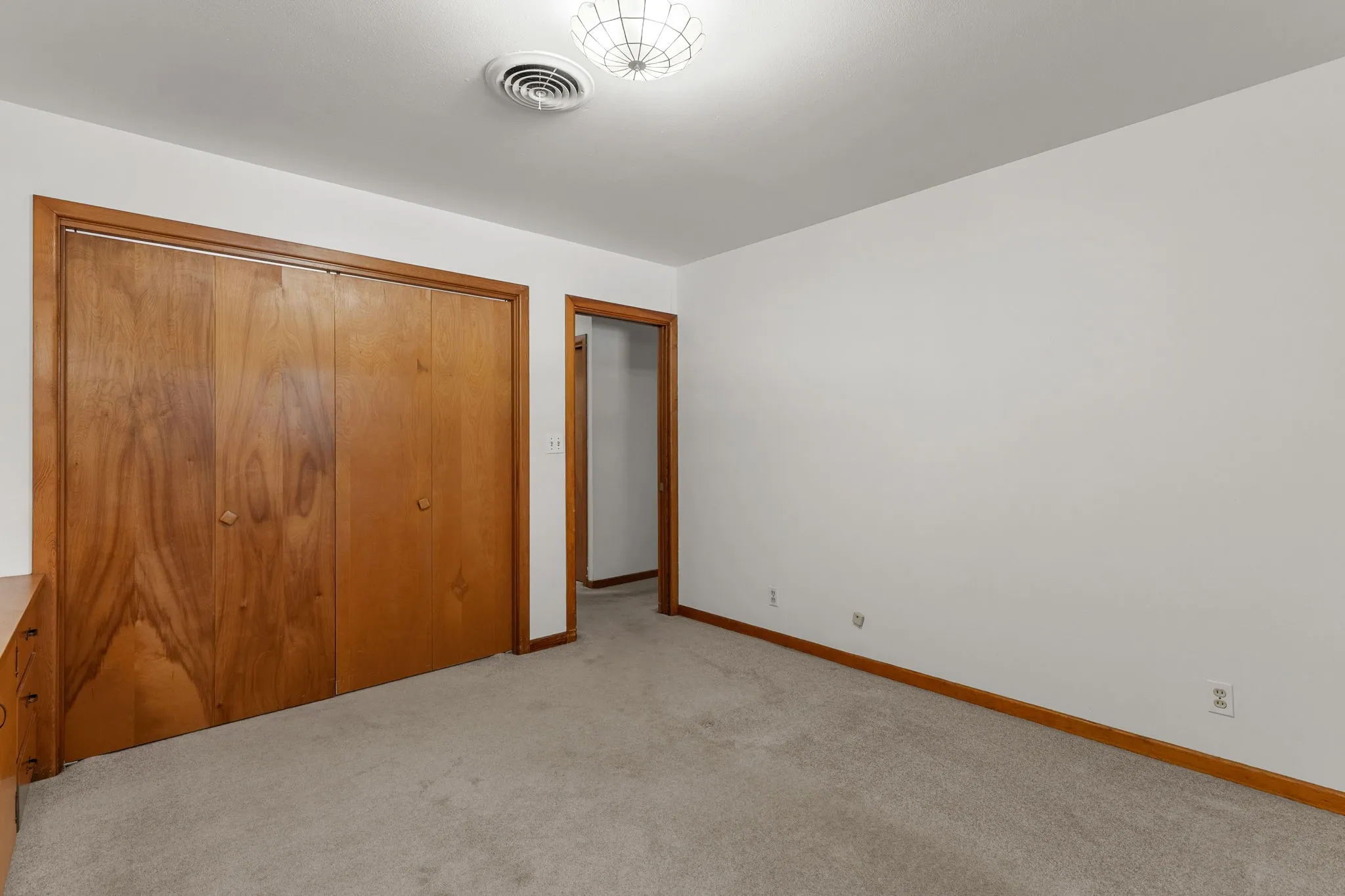Neutral carpet flooring, white painted walls, wood-finish bi-fold closet doors, and a flush mount ceiling light