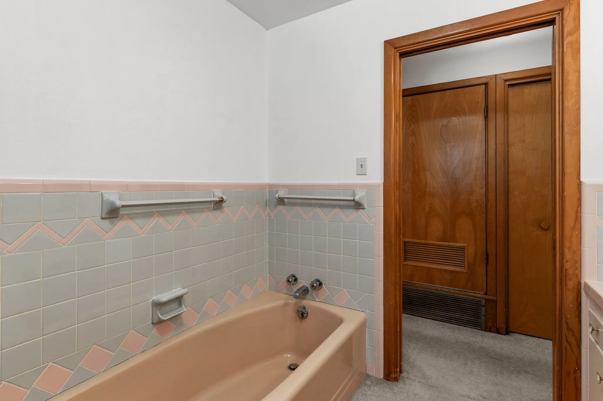 Bathroom featuring a peach-toned bathtub, tiled walls with decorative accents, and a wood-finished doorway