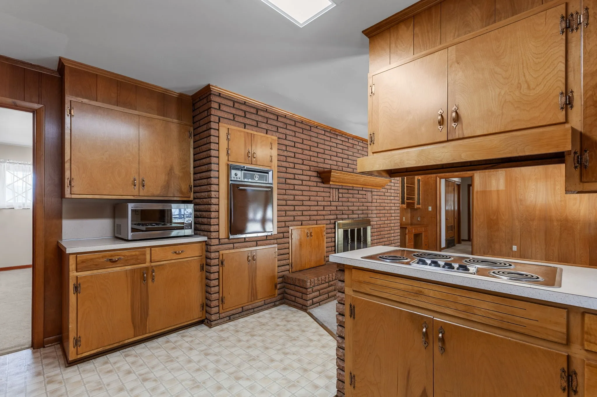 Kitchen featuring wood-paneled walls, built-in oven, integrated cooktop, and warm wood cabinetry