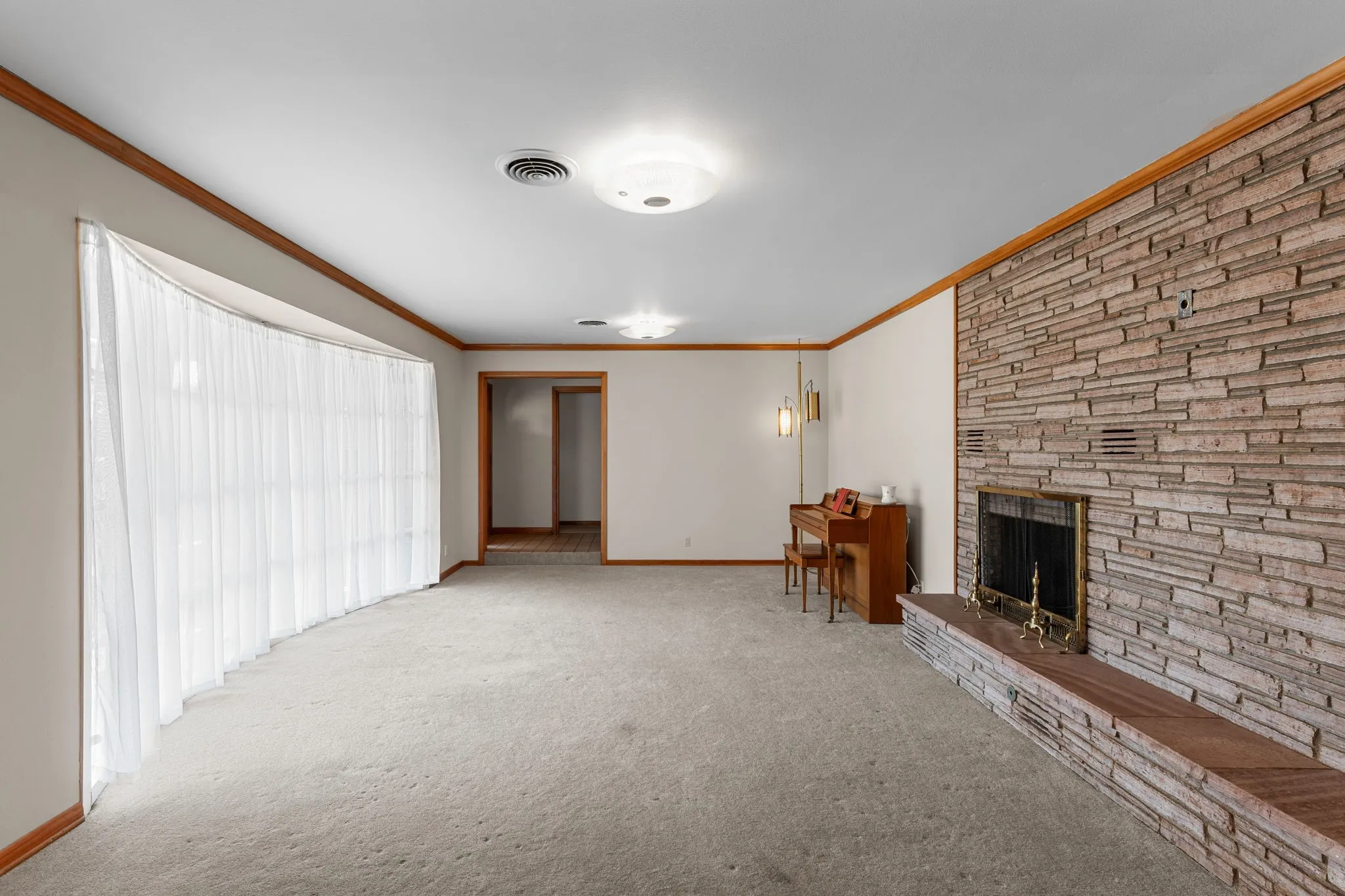 Spacious living area featuring a stone-clad fireplace with a hearth, wall-to-wall carpeting, and wood trim accents