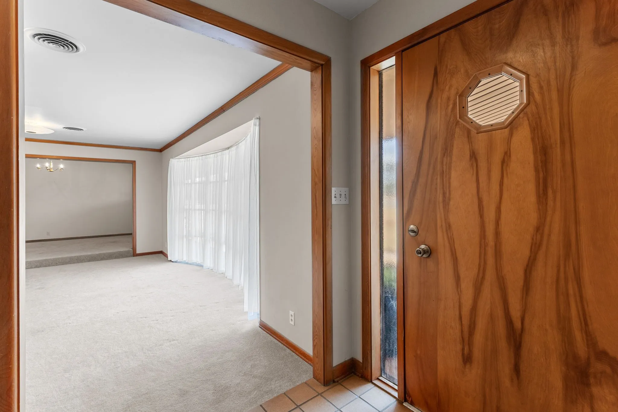 Wood-paneled entry door with an octagonal louvered accent and a full-length sidelight