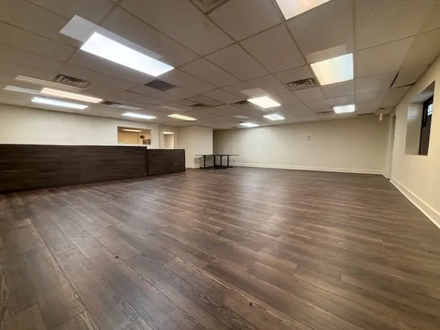 Expansive open space with wood-finish flooring, drop ceiling with integrated lighting, and a built-in wood-paneled counter