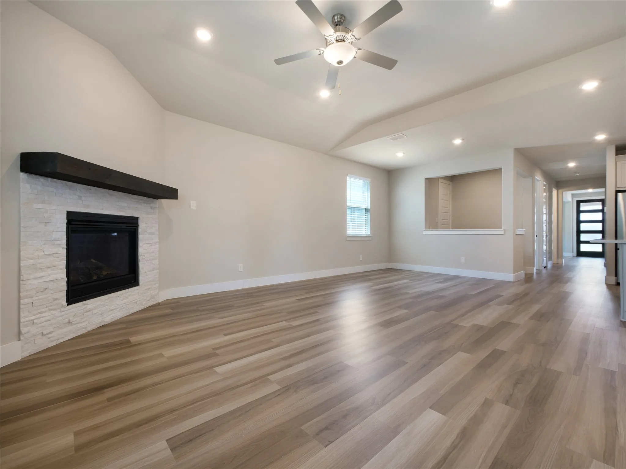 Vaulted ceiling, recessed lighting, wood-finish flooring, fireplace with stone surround, and ceiling fan