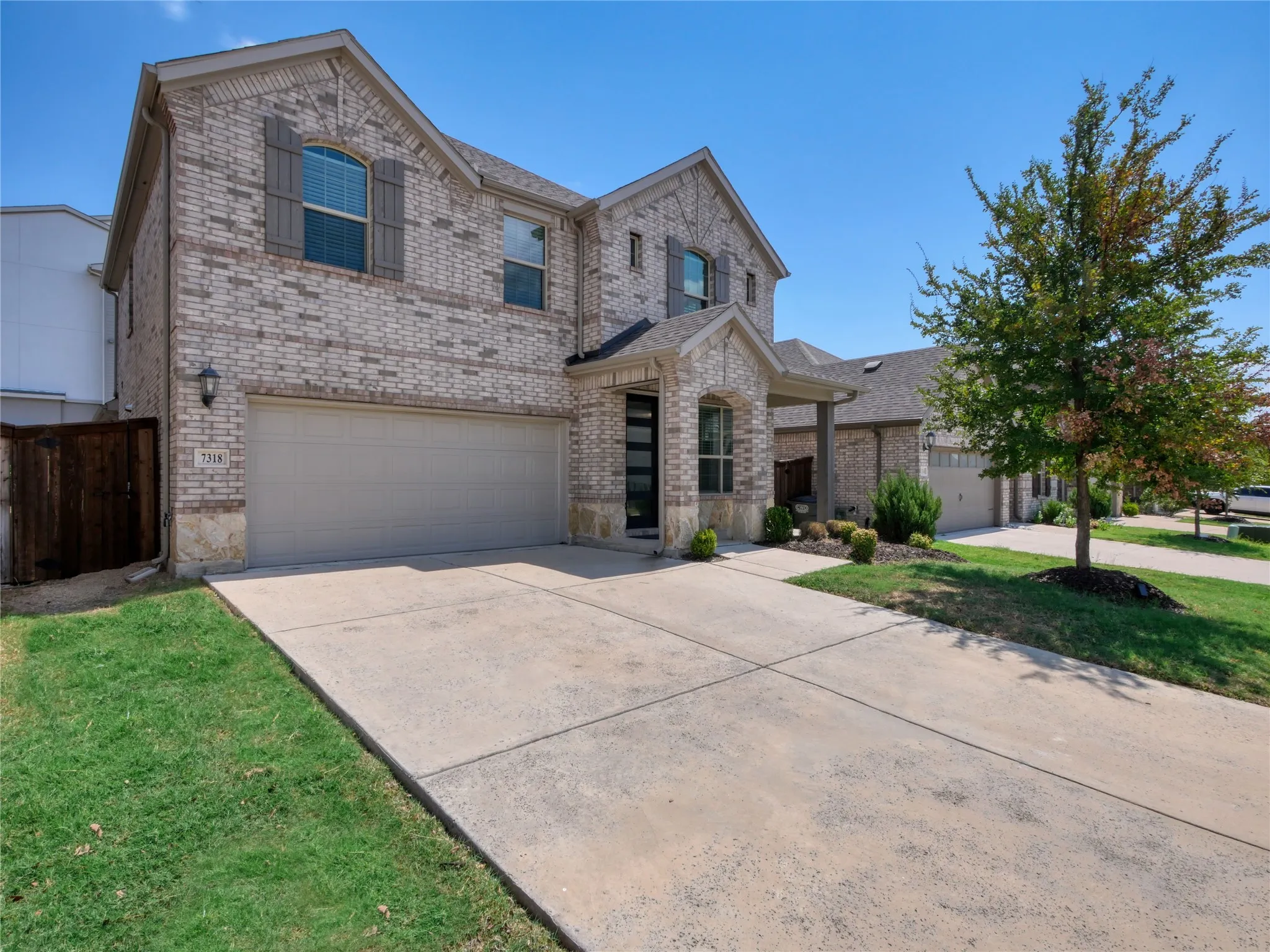Two-story residence featuring a light brick exterior with stone accents, a two-car garage, and a covered entry