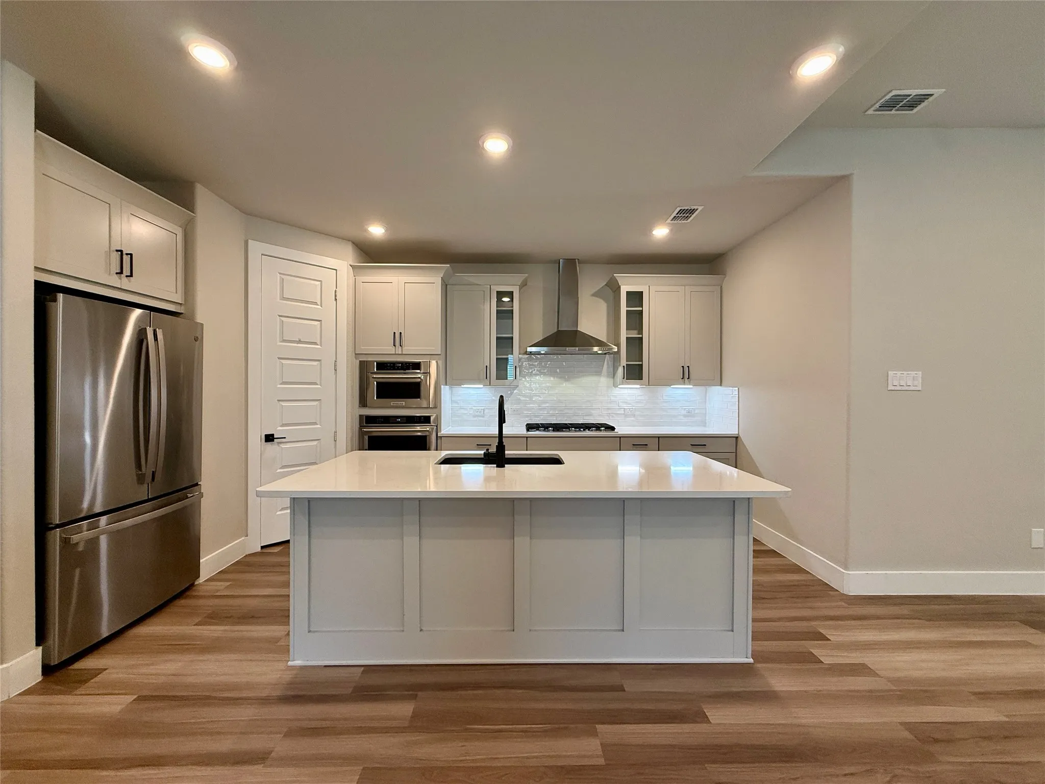 Kitchen featuring light gray cabinets, a central island with a sink, stainless steel KitchenAid appliances, under cabinet lighting, subway tile backsplash, and walk in pantry.