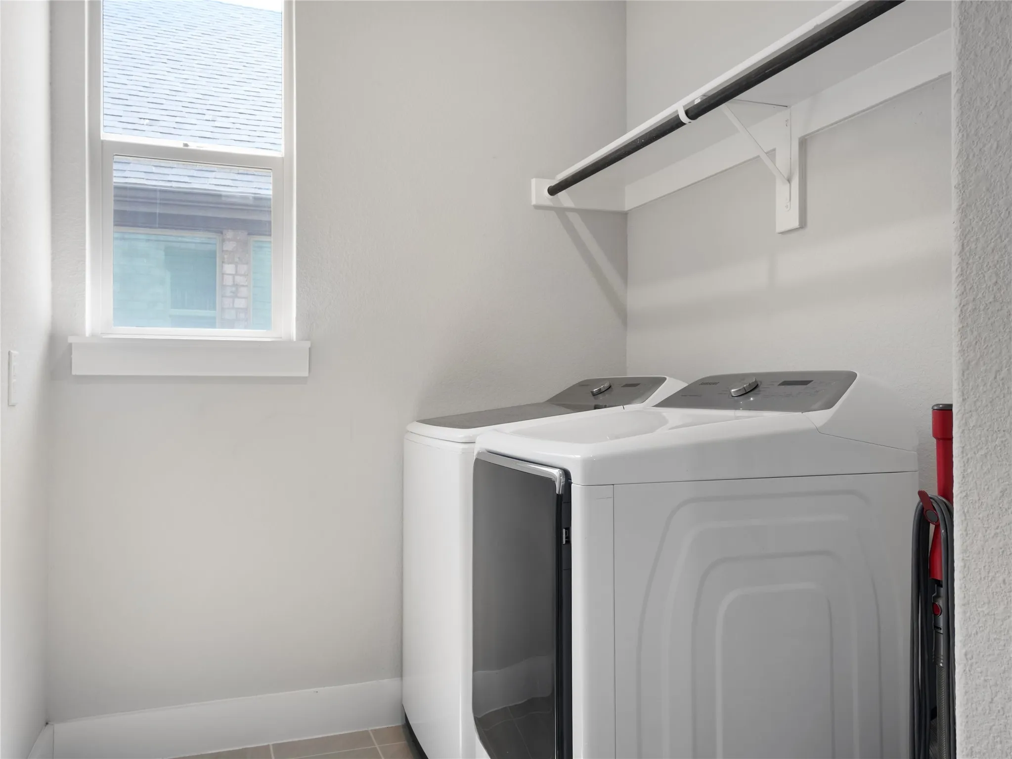 Utility space with a window, tile flooring, and a mounted shelf with a hanging rod