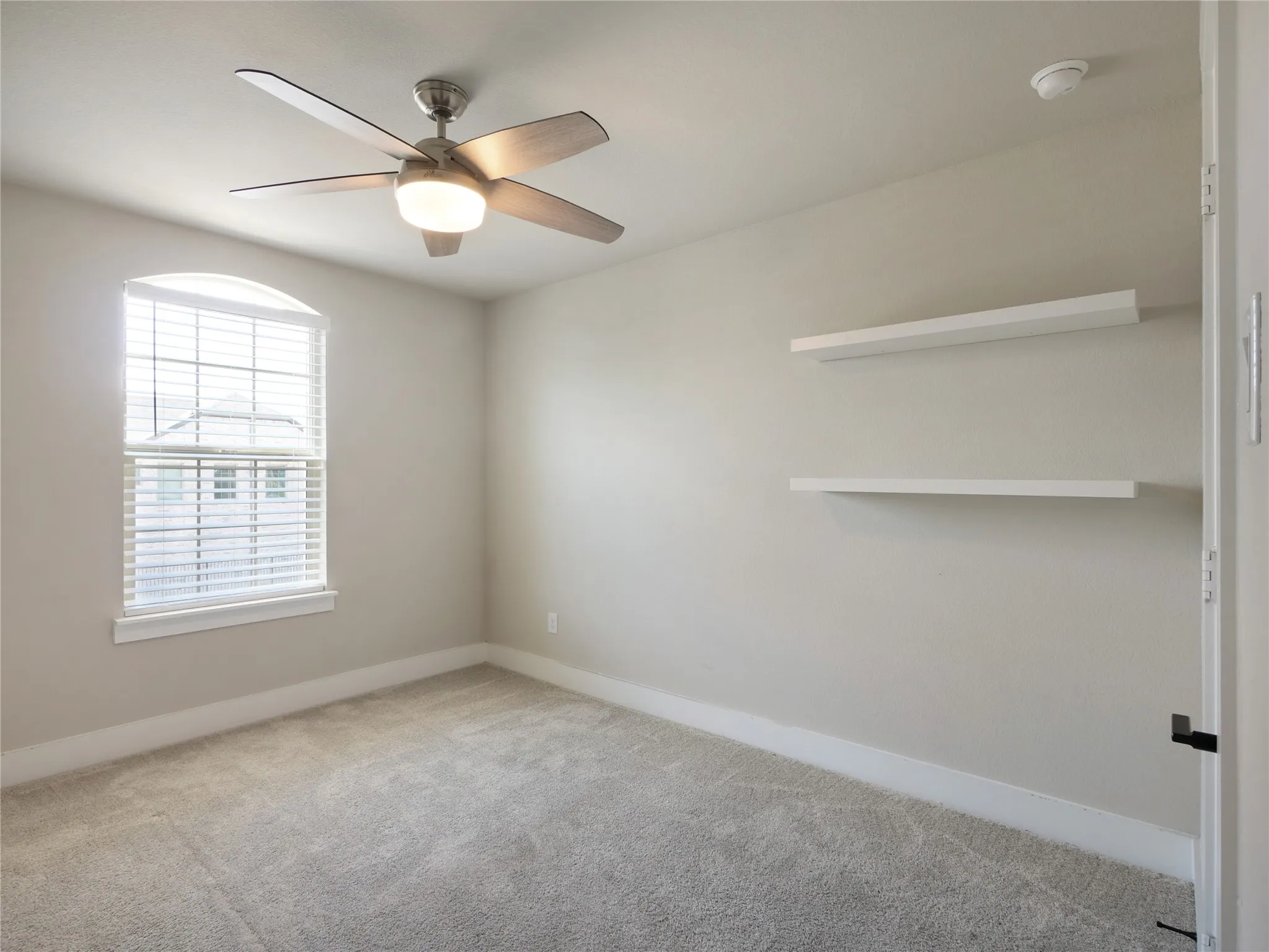 Bedroom 1 has arched window with blinds, ceiling fan and two wall-mounted shelves, and carpeted flooring