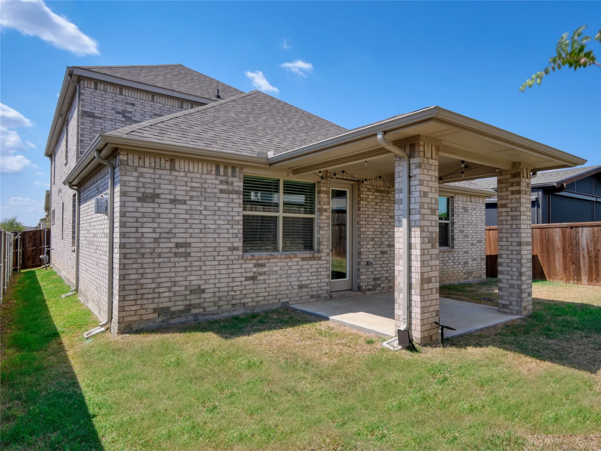 Covered patio with brick columns, concrete flooring, and an exterior door