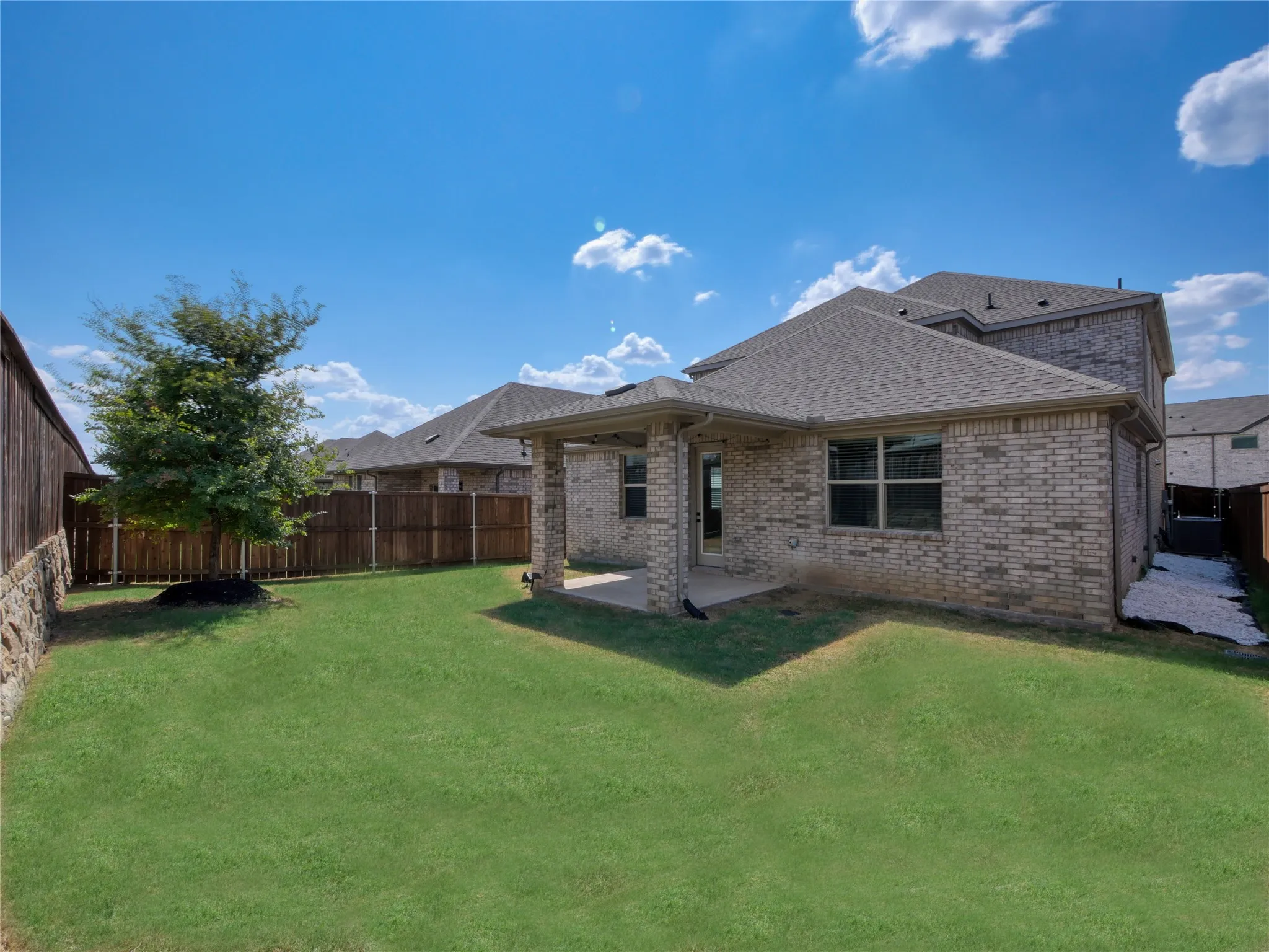 Back yard has an oak tree, covered back porch, bordered by a wood fence and a stone retaining wall