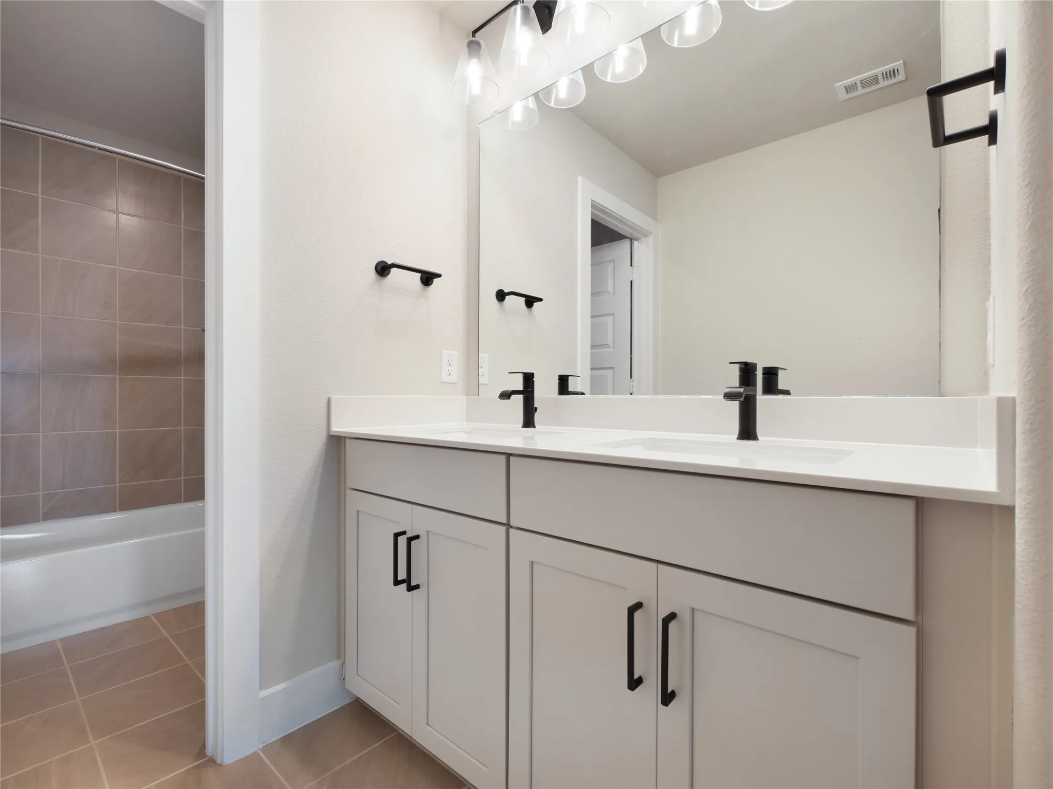 Hall Bathroom with dual vanity with white countertop, matte black hardware, and overhead lighting. Bathing area in a separate room.