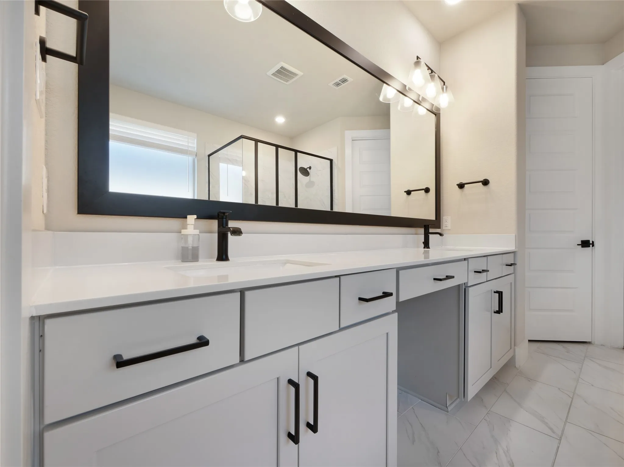 Dual vanity with light gray cabinetry, matte black hardware, and an expansive framed mirror