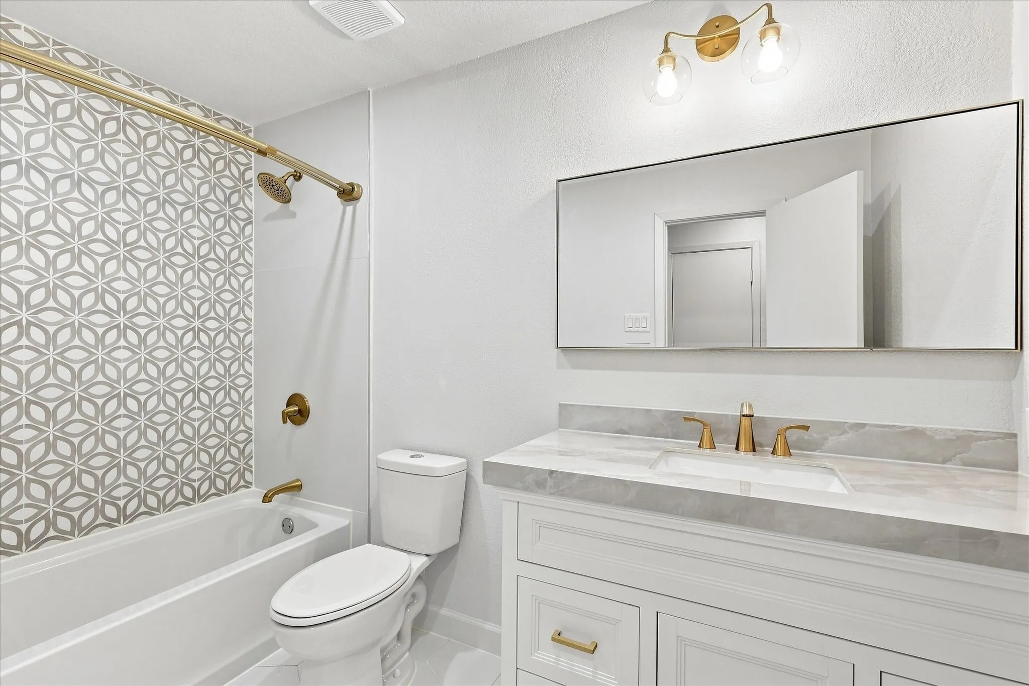 Spa-inspired bathroom featuring a floating vanity with quartz countertop, brass fixtures, and an expansive mirror with integrated lighting