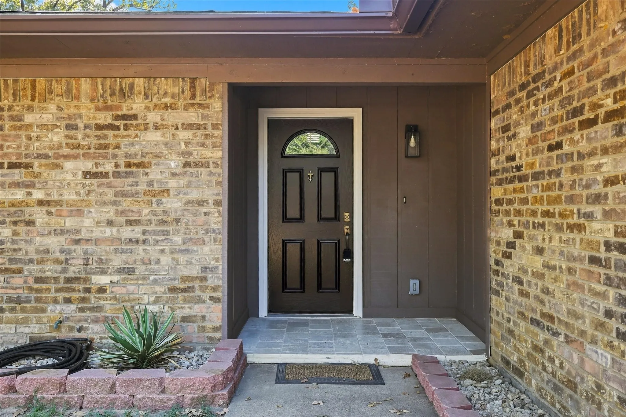 Brick exterior with a dark-paneled entry door, arched transom window, and a tiled entry landing
