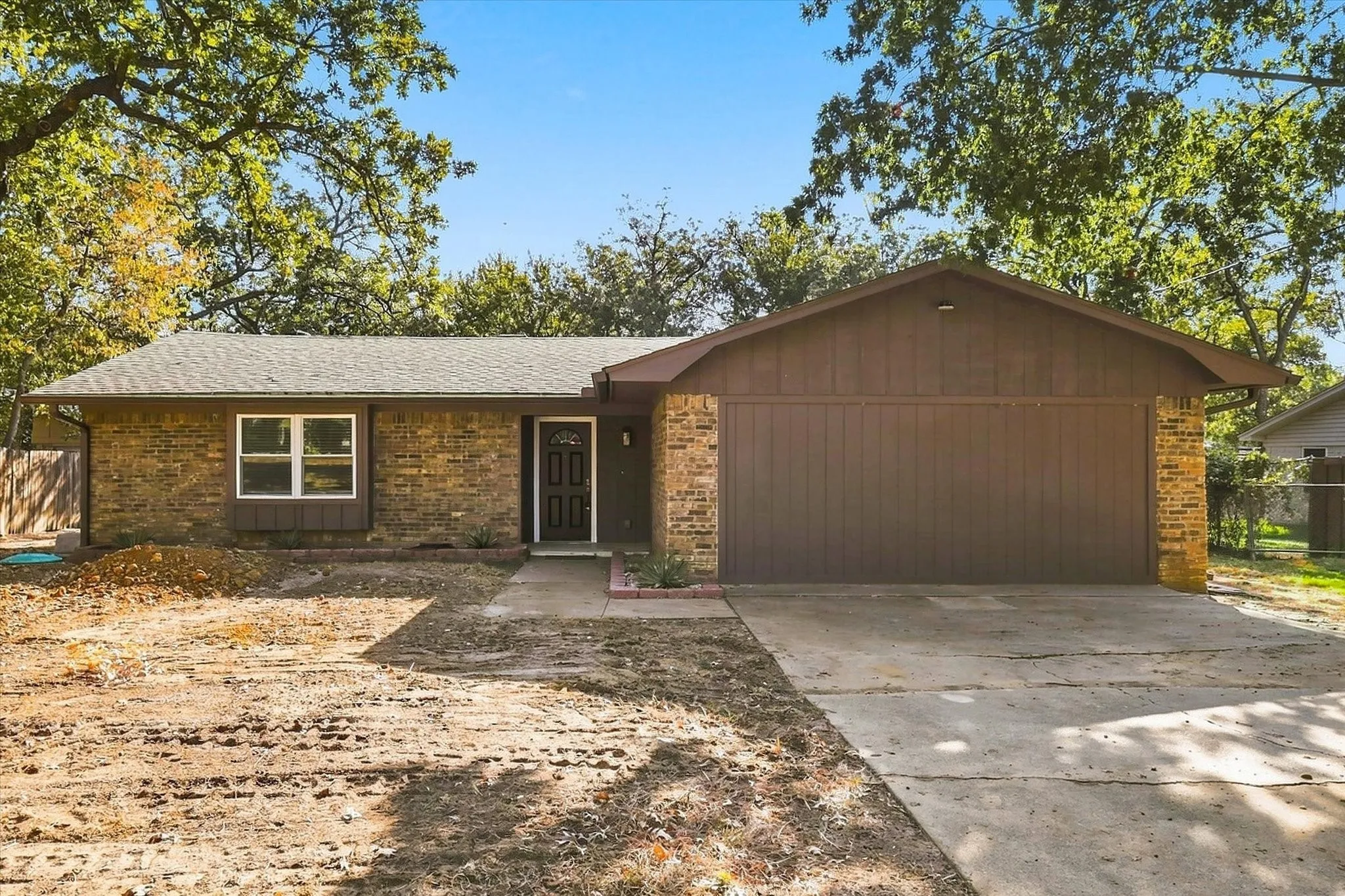 Brick and wood-sided exterior with an attached garage, a gabled roof, and a concrete driveway.