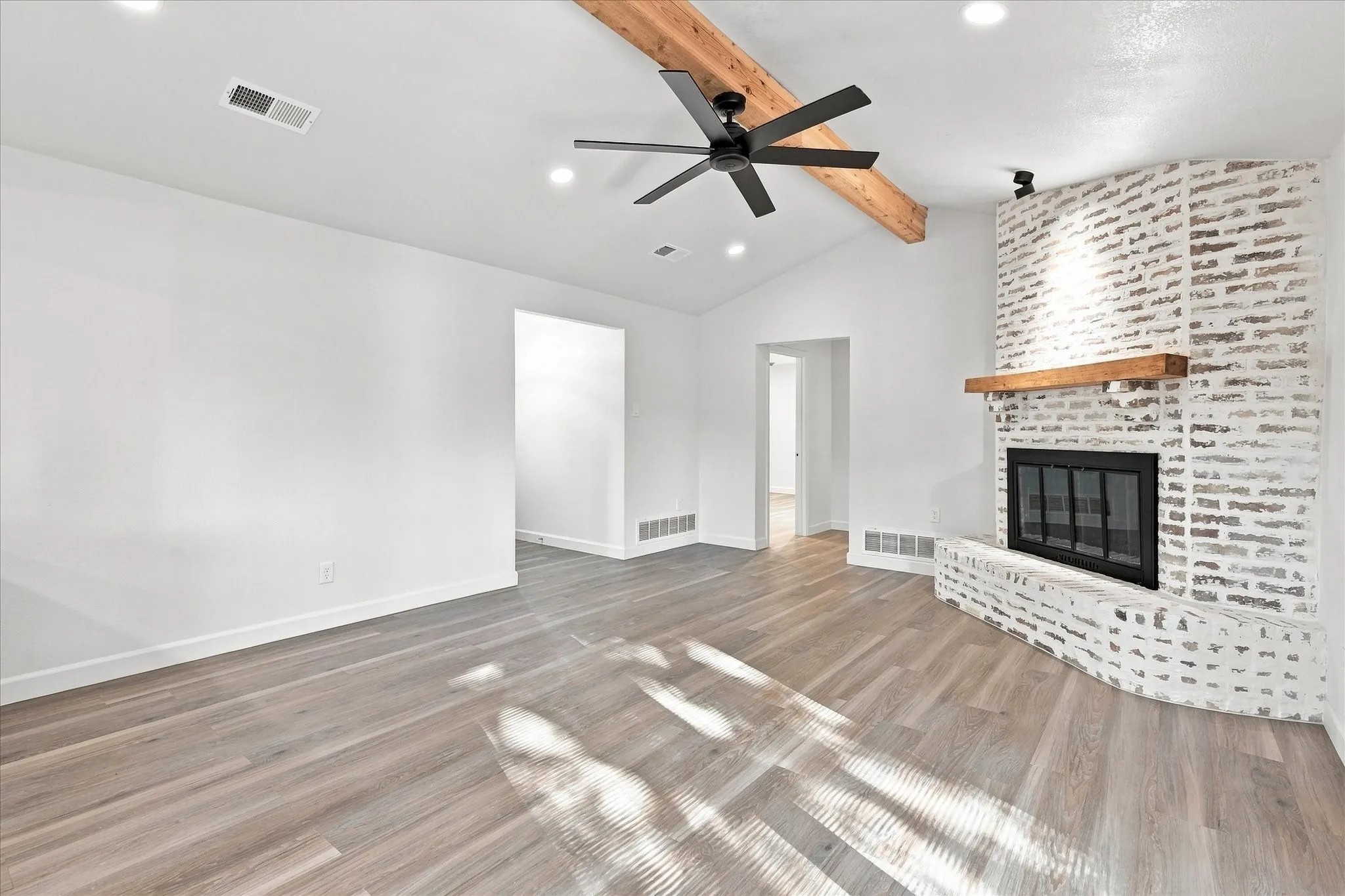 Vaulted ceiling with exposed wood beam, recessed lighting, wood-finish flooring, and a brick fireplace with a wood mantel