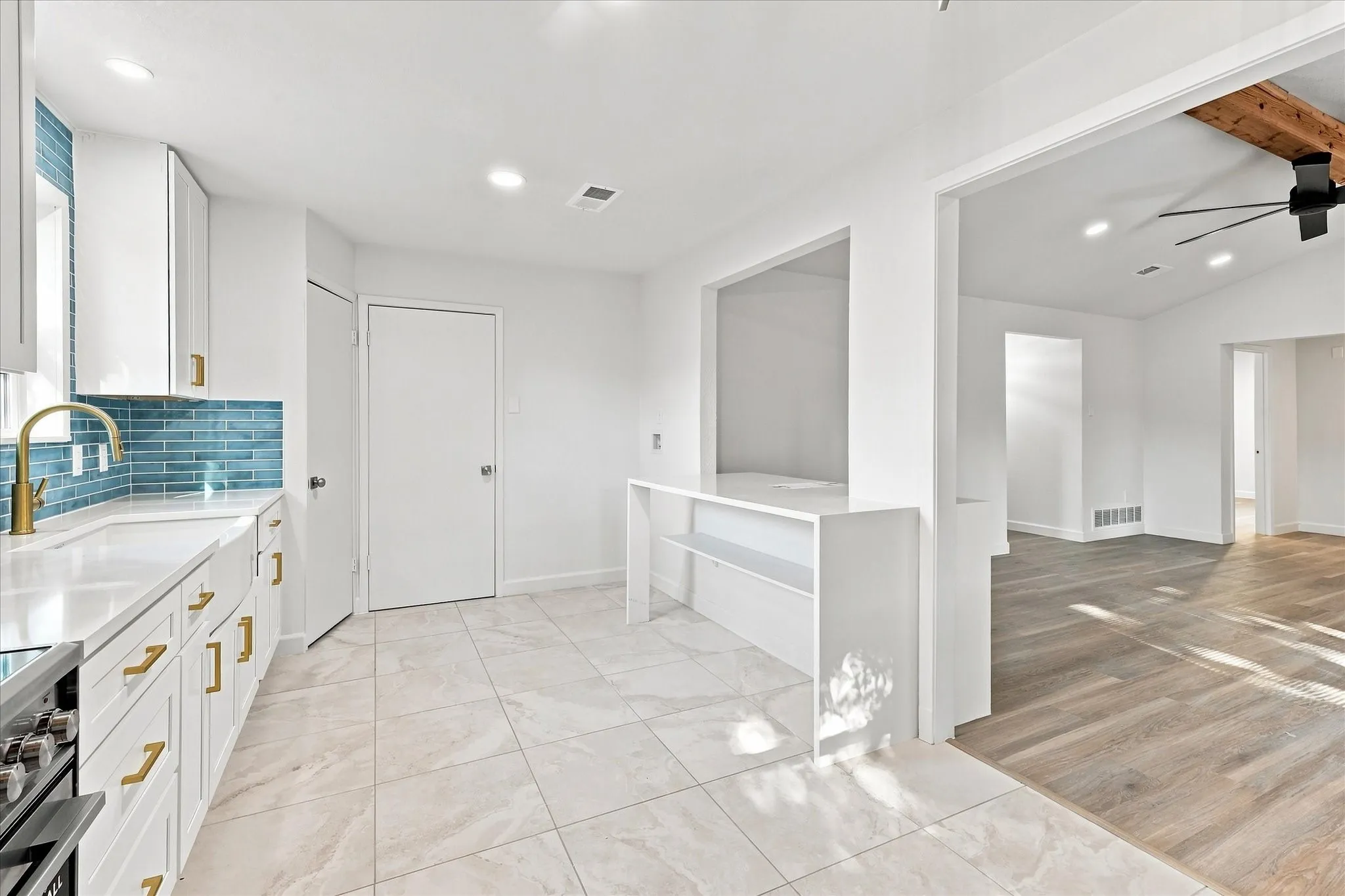 White kitchen cabinetry with gold-tone hardware, blue subway tile backsplash, and light-toned tile flooring