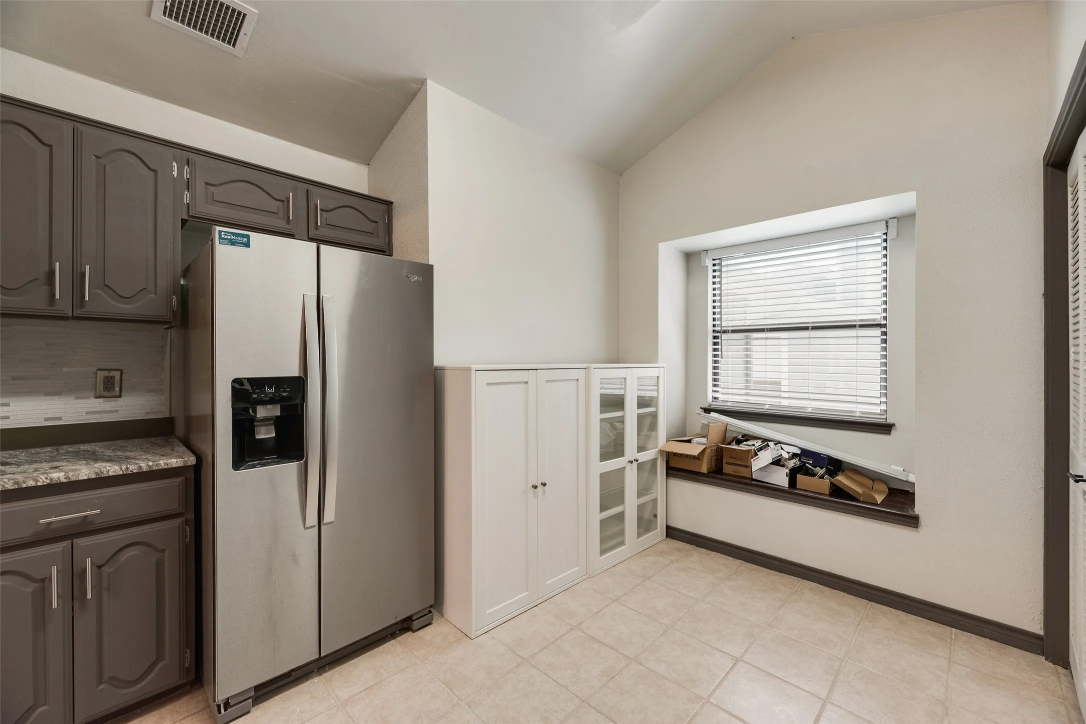 Vaulted ceiling, recessed window, tiled flooring, built-in cabinetry, and gray-painted wood cabinets
