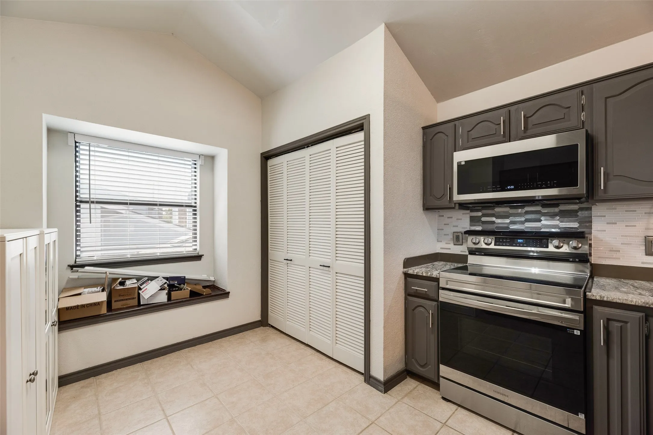 Stainless steel appliance suite, gray cabinetry, tile backsplash, and louvered closet doors