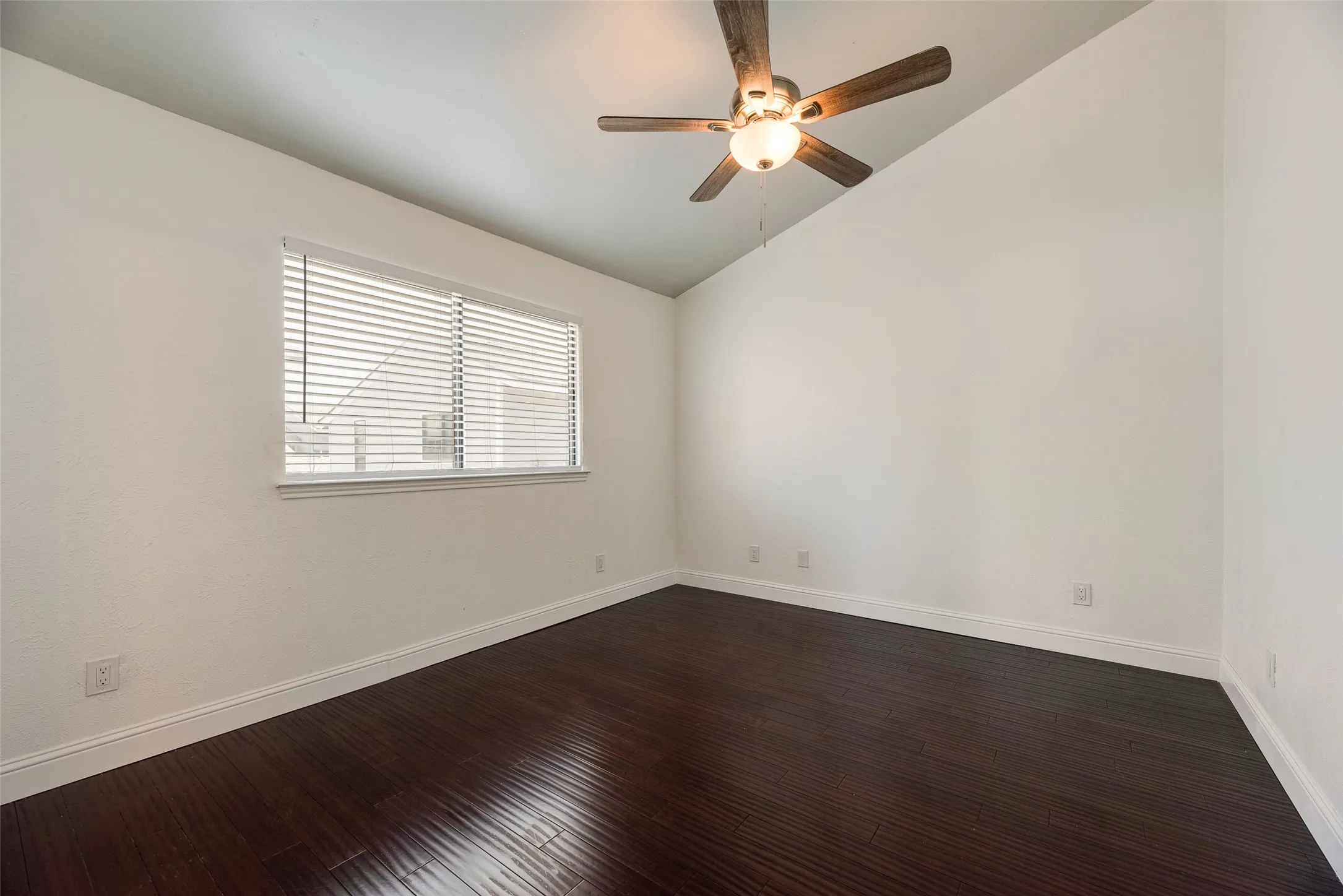Vaulted ceiling featuring a ceiling fan with integrated lighting, wood-finish flooring, and window with horizontal blinds