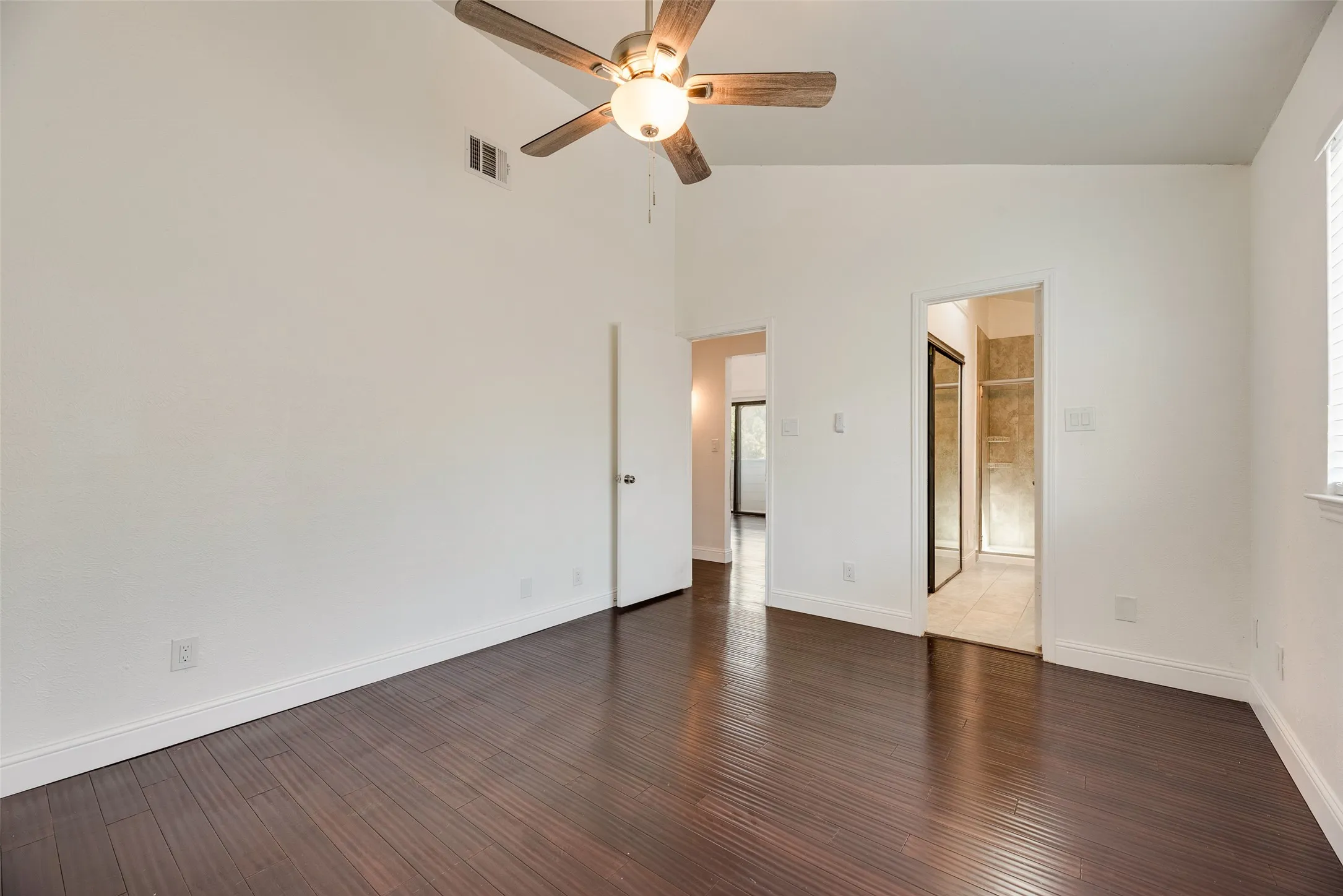 Vaulted ceiling with an attached ceiling fan, dark wood-finish flooring, white baseboards, and doorways to other interior spaces