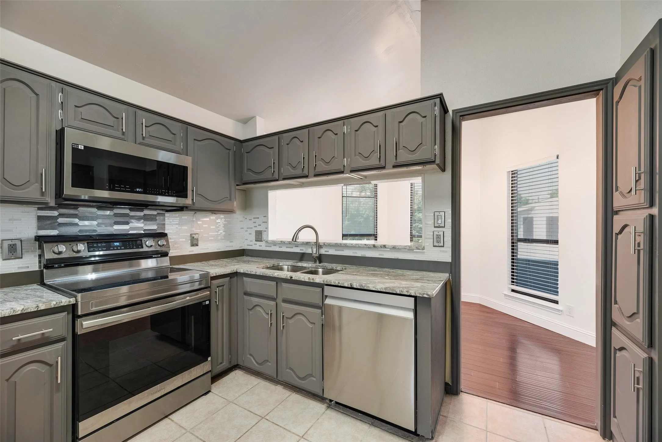 Kitchen featuring gray cabinetry, stainless steel appliances, a tile backsplash, and a double basin sink