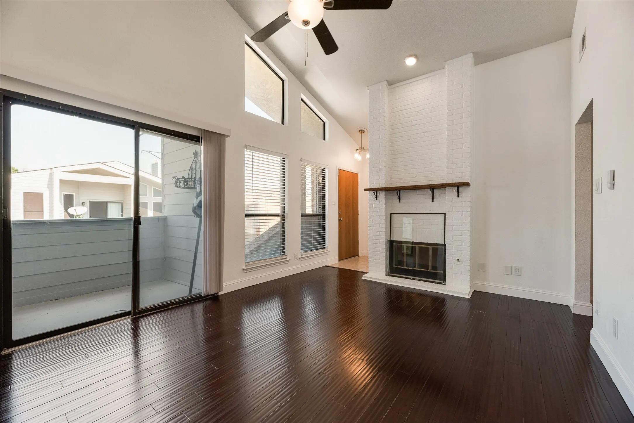 Vaulted ceilings, dark wood-finish flooring, and a white brick fireplace with a wood mantle