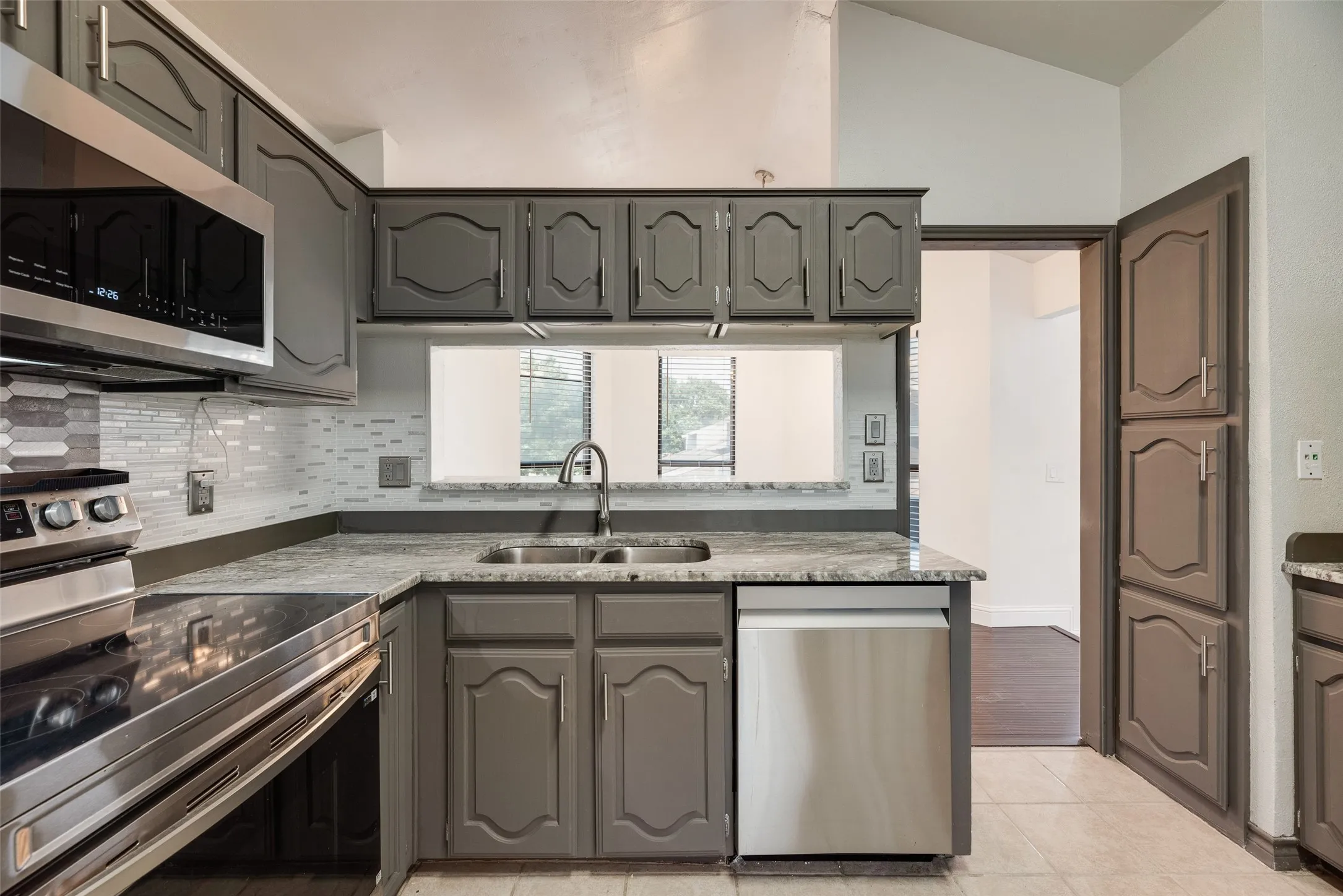 Kitchen featuring gray cabinetry, stainless steel appliances, granite-look countertops, and a mosaic tile backsplash
