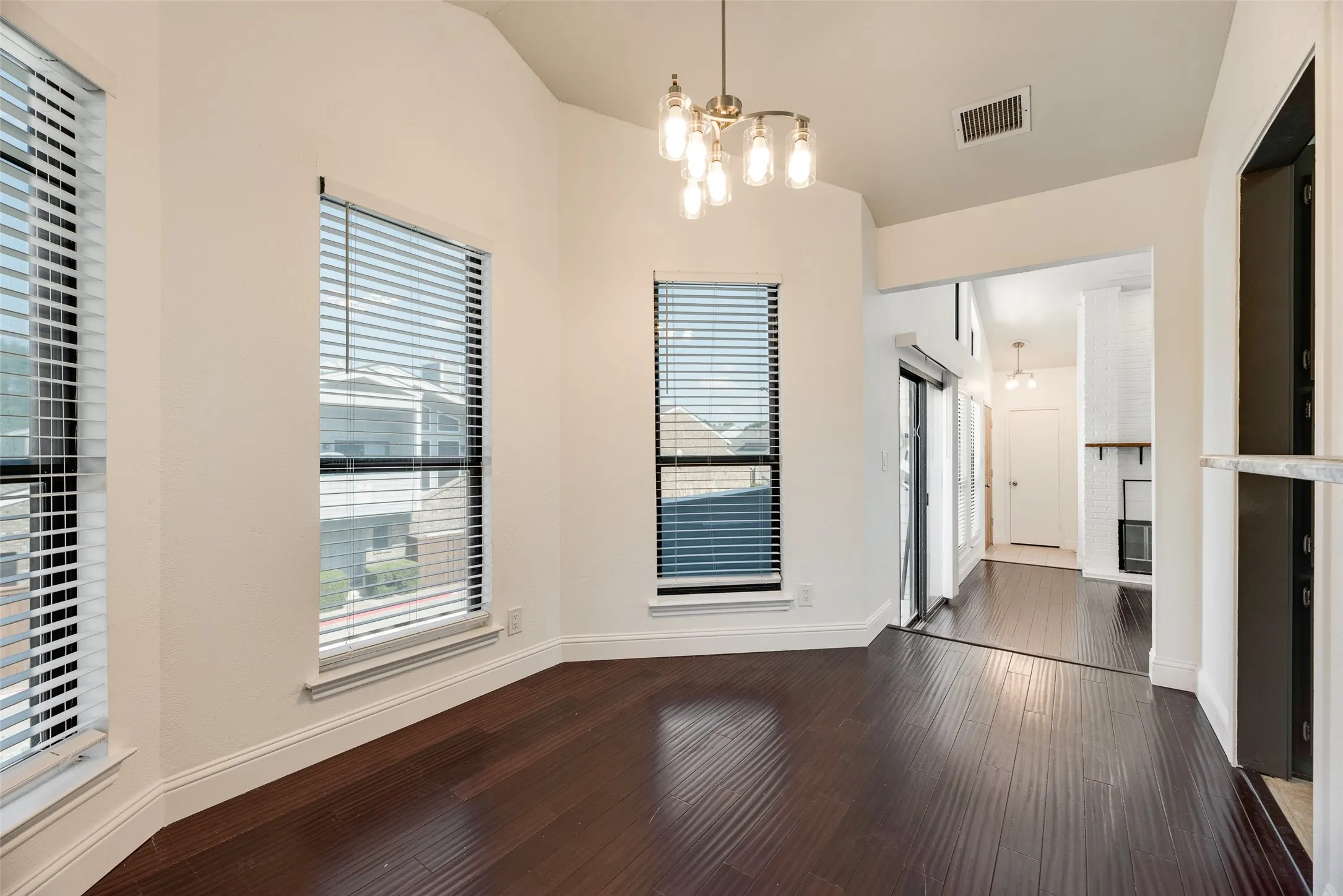 Vaulted ceiling, dark wood-finish flooring, two large windows with blinds, recessed lighting, and a modern brass chandelier