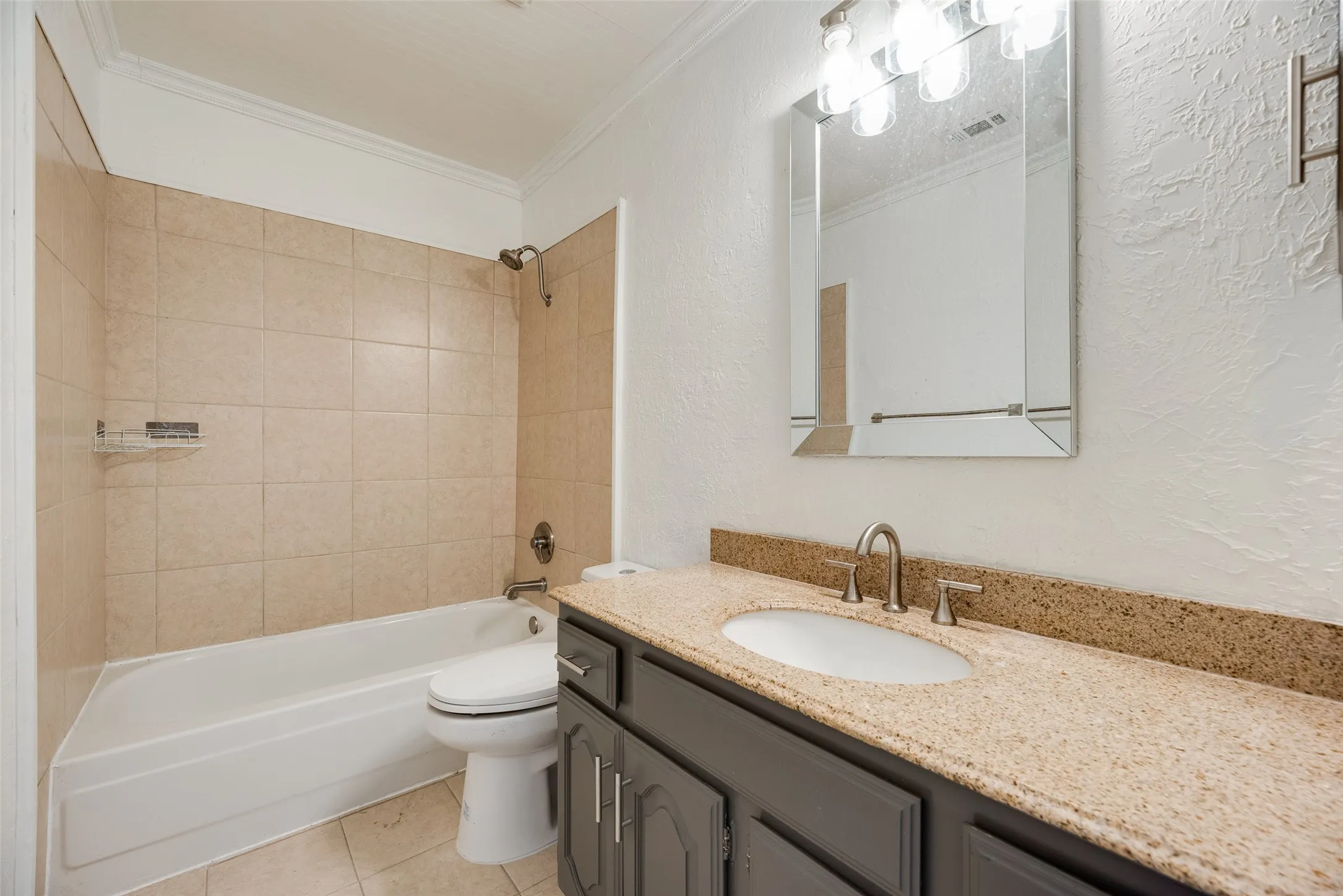 Bathroom featuring a bathtub with tiled surround, a vanity with a light-colored countertop, and a framed mirror with overhead lighting