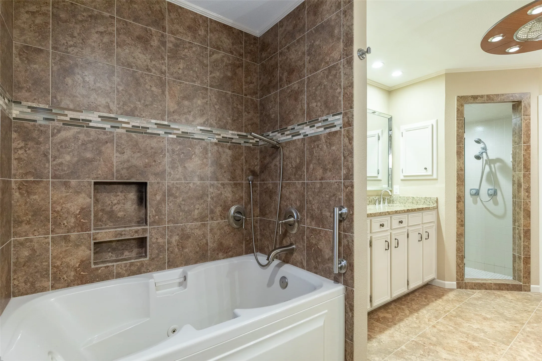 Jetted tub with brown tile surround and mosaic accent