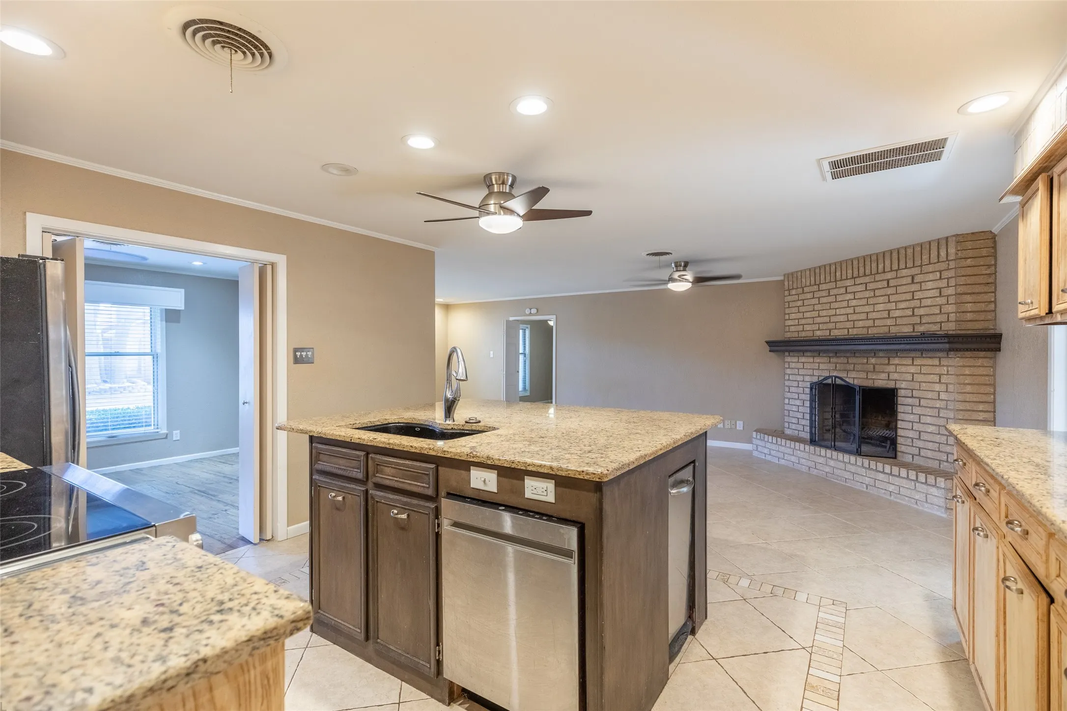Kitchen island with integrated sink and dishwasher, granite countertops, tile flooring, and brick fireplace with mantle