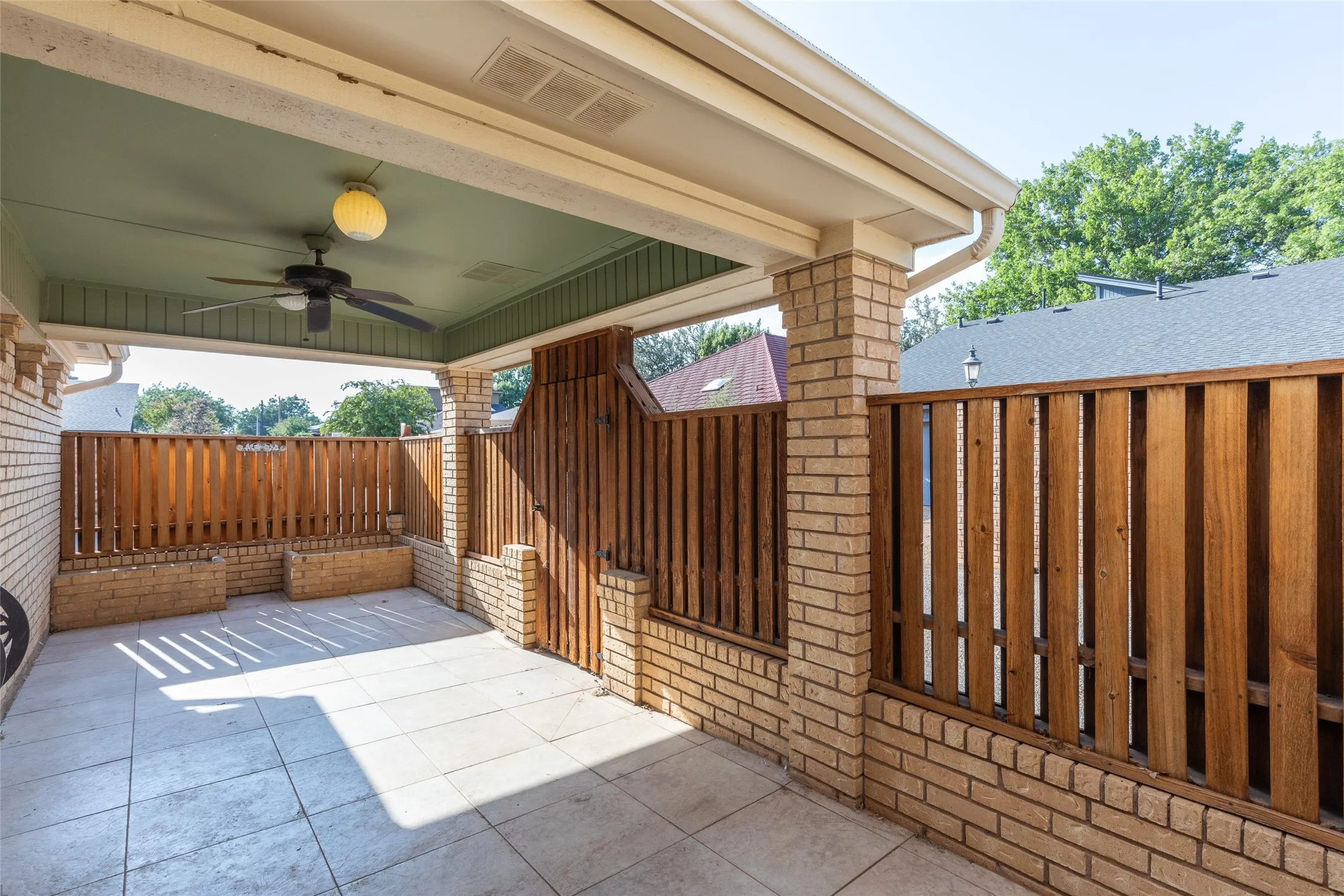 Covered patio featuring a ceiling fan, recessed lighting, brick columns, and wood panel fencing