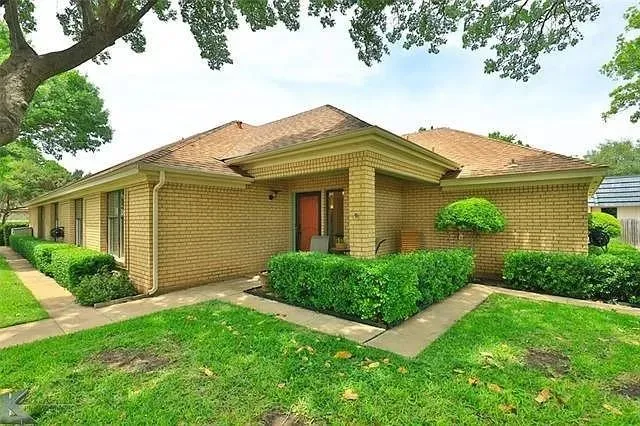 Brick exterior with covered entry, concrete walkway, and manicured landscaping