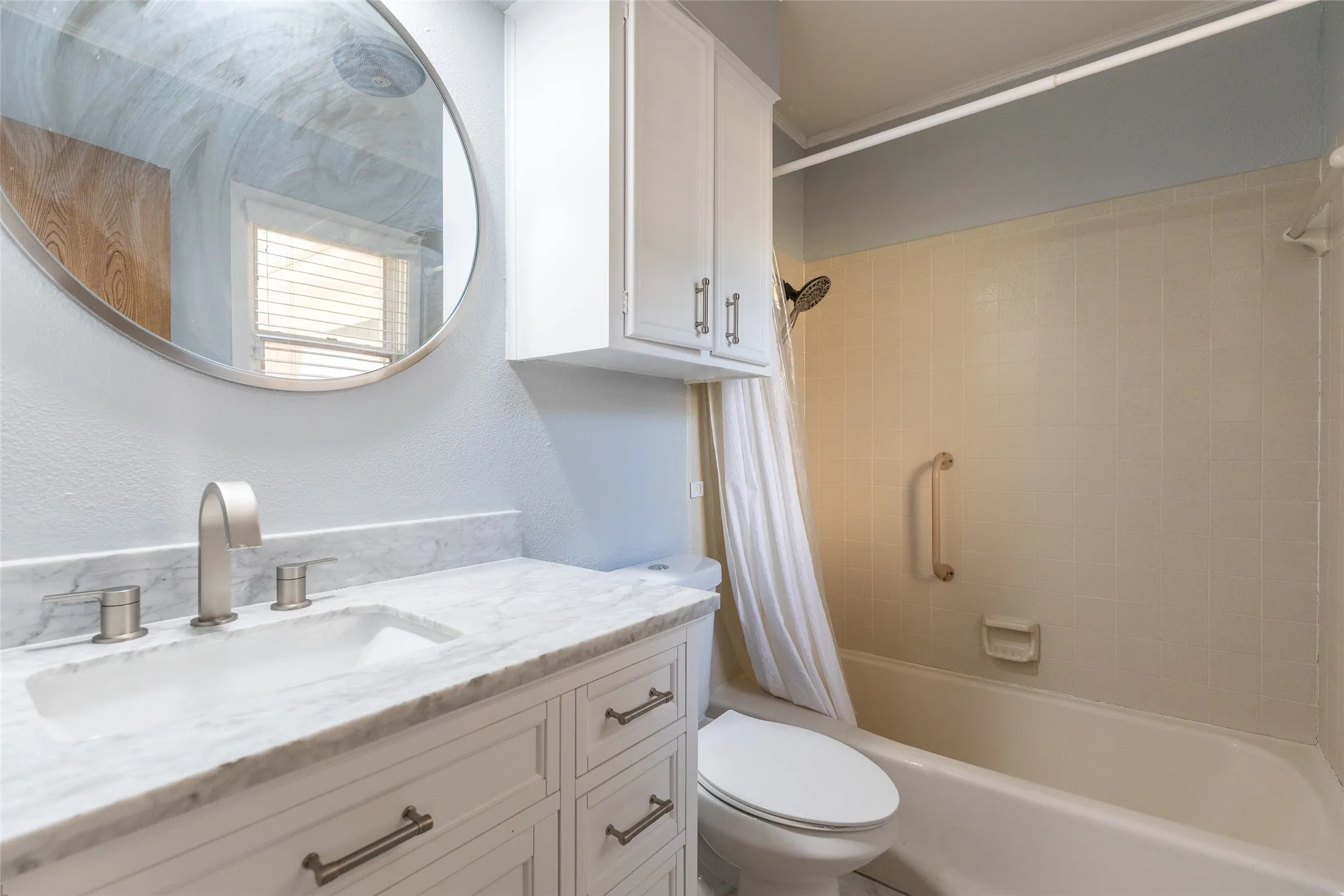 Vanity with a marble-look countertop and white shaker-style cabinetry, undermount sink with a brushed nickel faucet, and a round frameless mirror