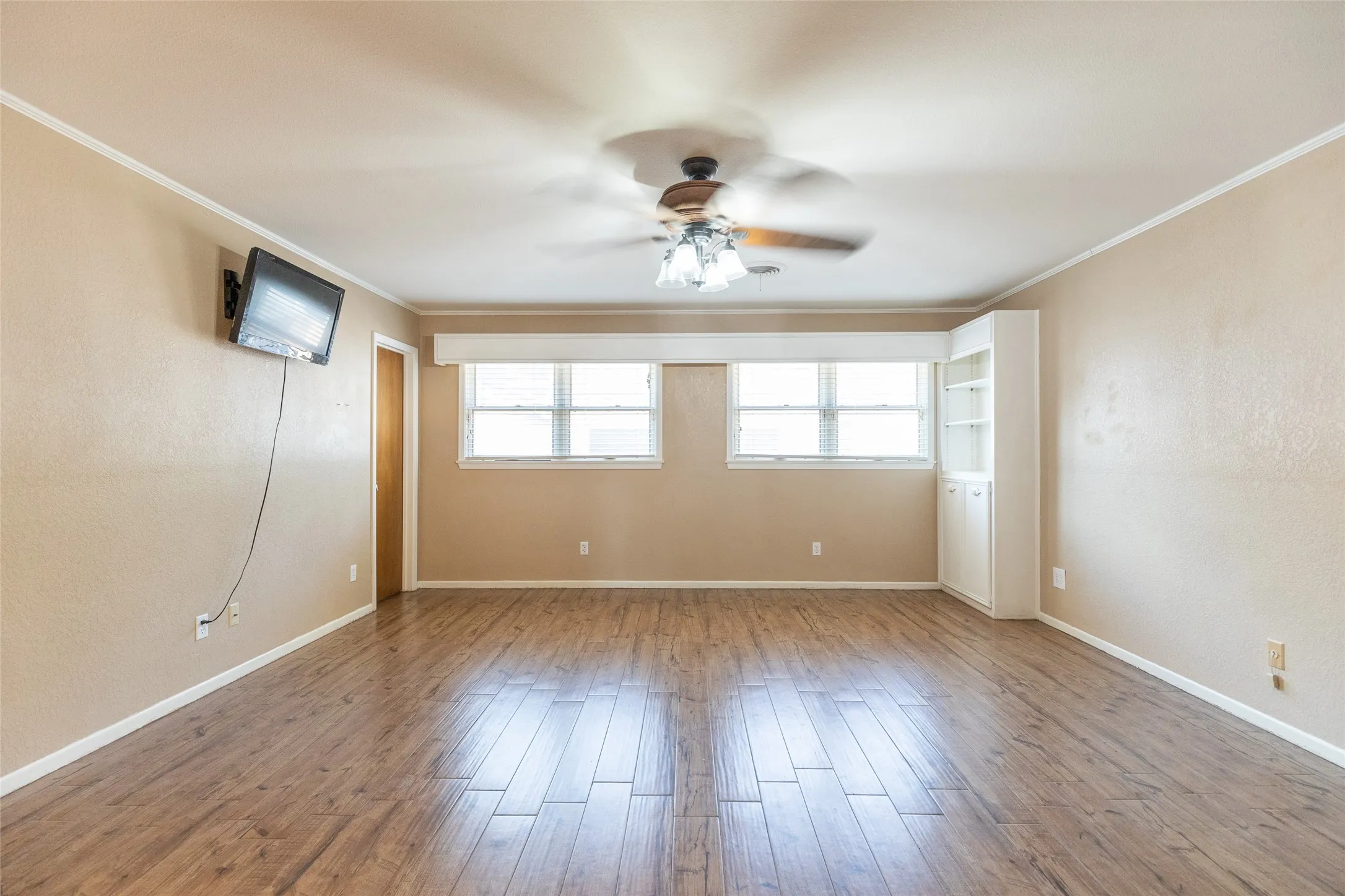 Wood-finish flooring, dual windows with blinds, built-in shelving, and a ceiling fan with integrated lighting