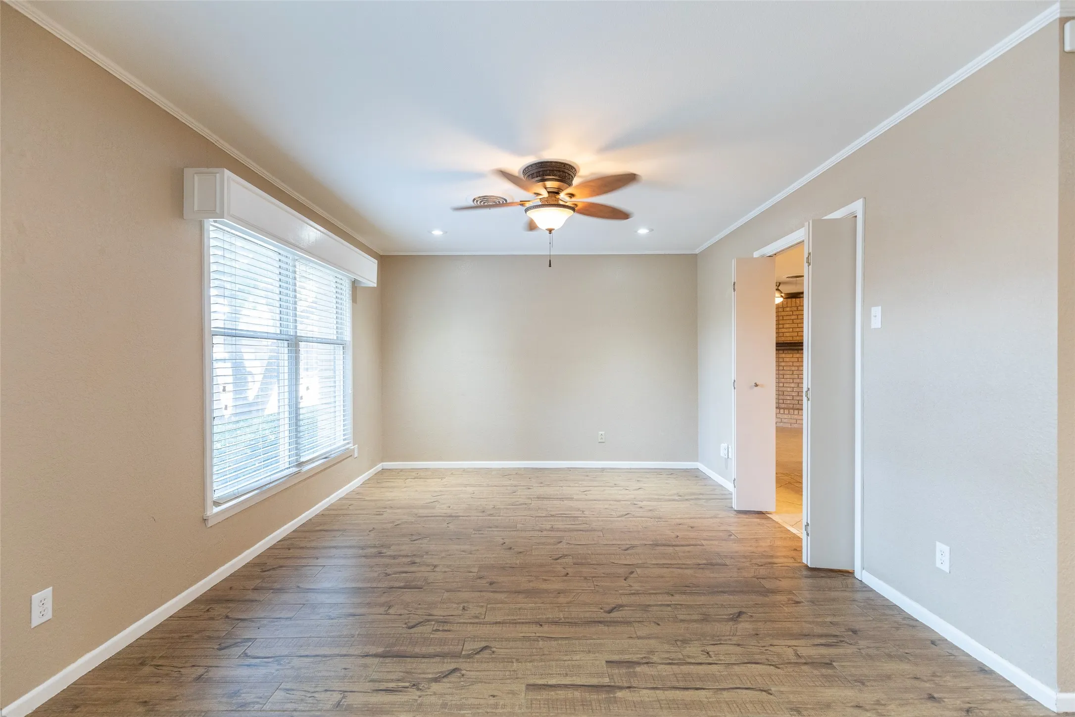 Wood-finish flooring, ceiling fan, recessed lighting, double window with blinds, and white trim throughout