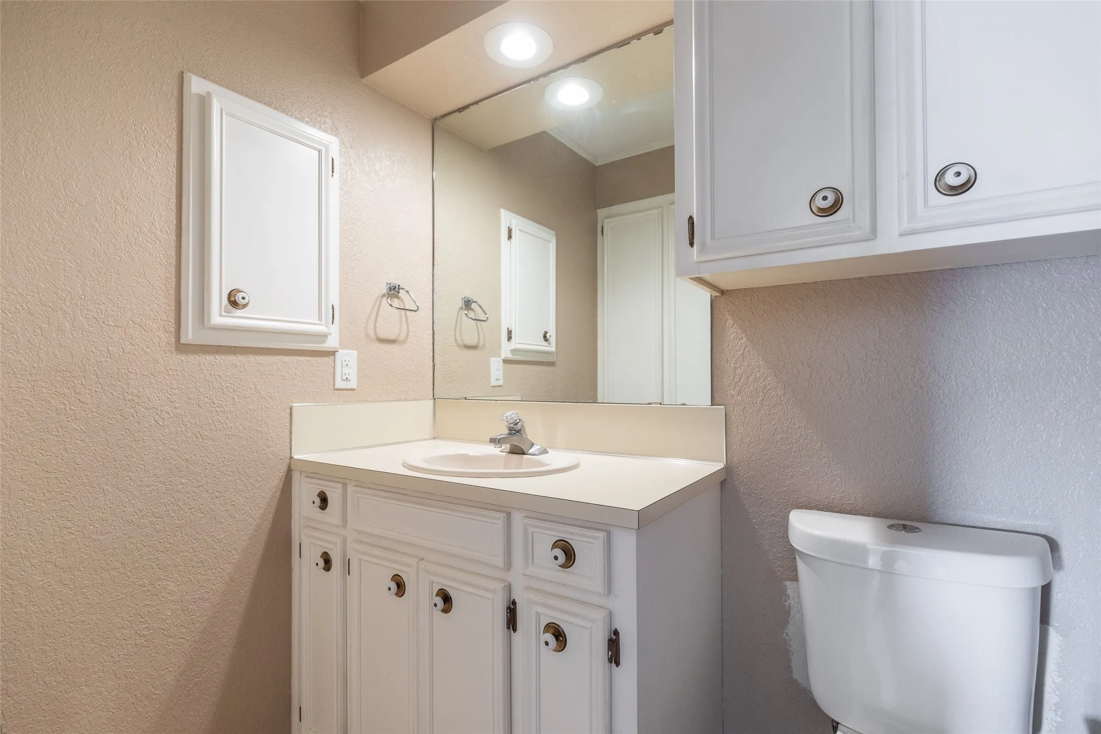 Vanity with an integrated sink and countertop, white cabinetry with decorative hardware, and a mirrored wall
