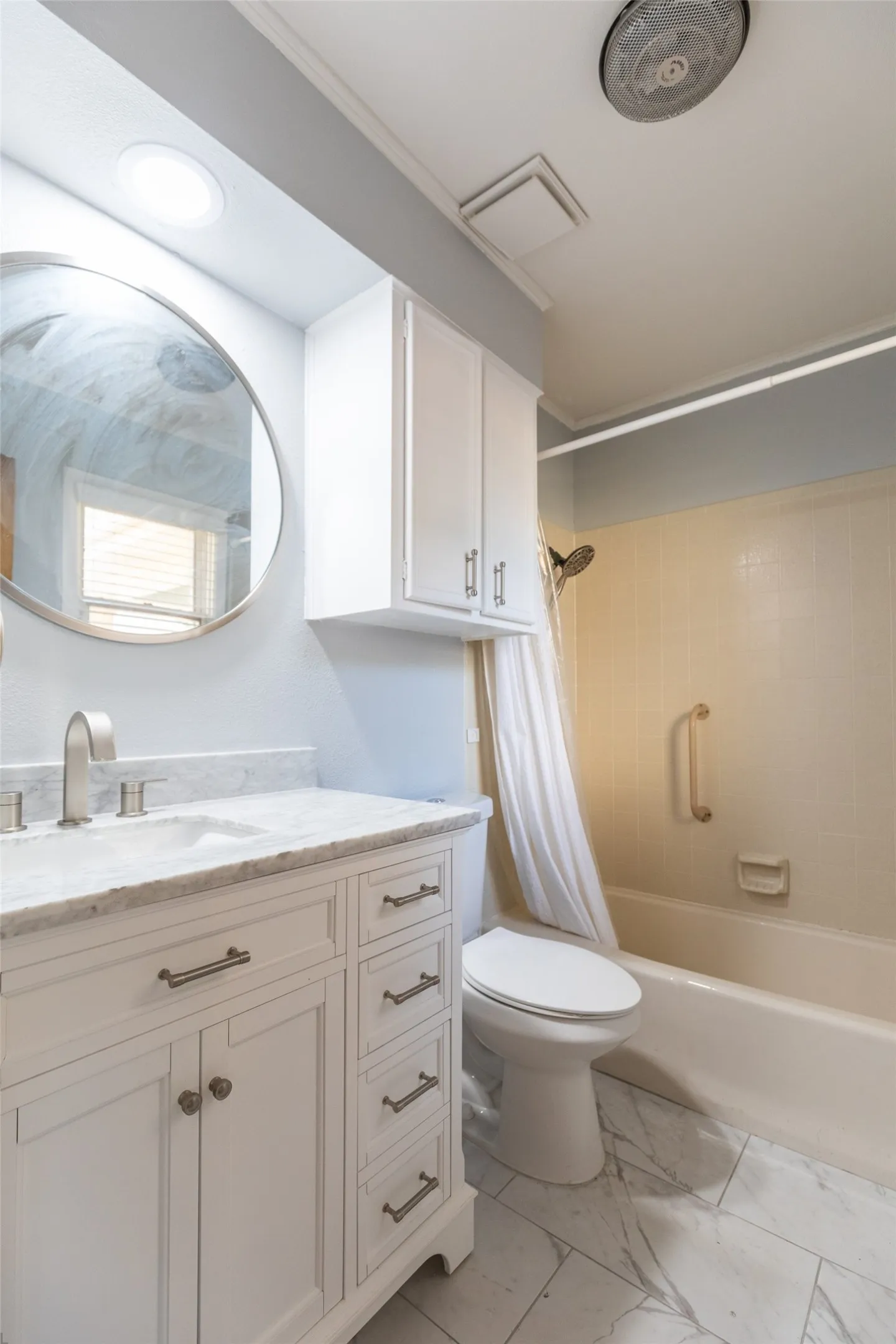 White vanity with a stone countertop and integrated sink, brushed nickel faucet, large round mirror, and tile flooring