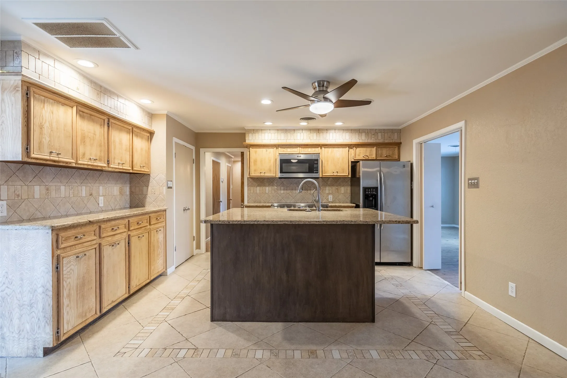 Kitchen featuring a central island, light wood-finish cabinetry, tile backsplash, and stainless steel appliances