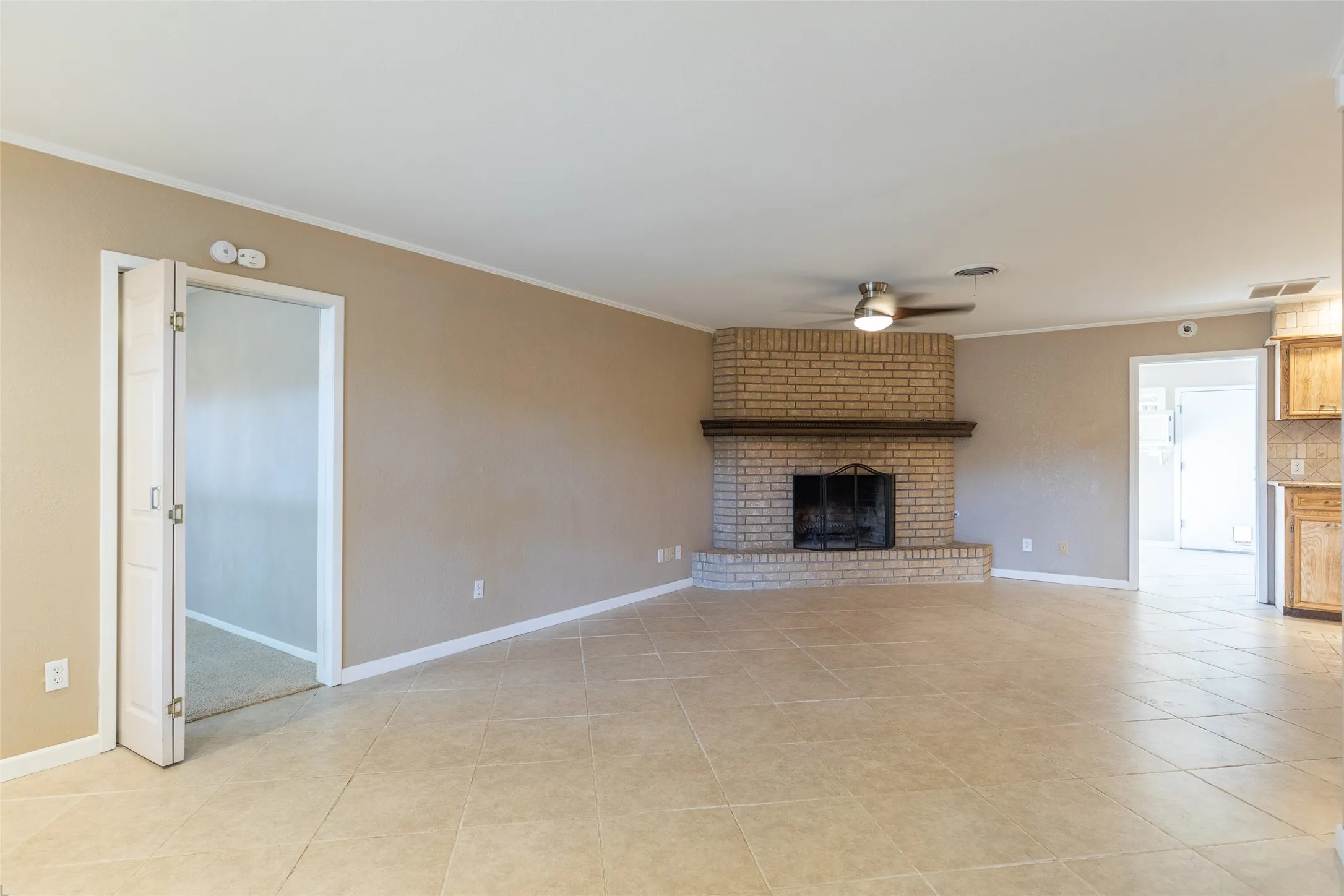 Spacious living area featuring neutral tile flooring, a brick fireplace with a wood mantle, and a ceiling fan