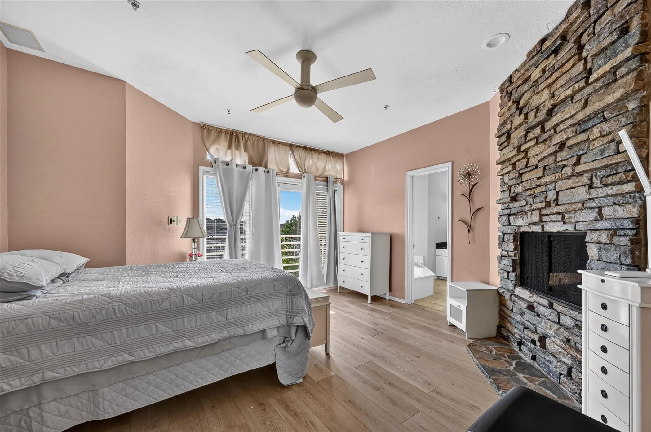 Stone-clad fireplace with hearth, wood-finish flooring, ceiling fan, recessed lighting, and balcony access